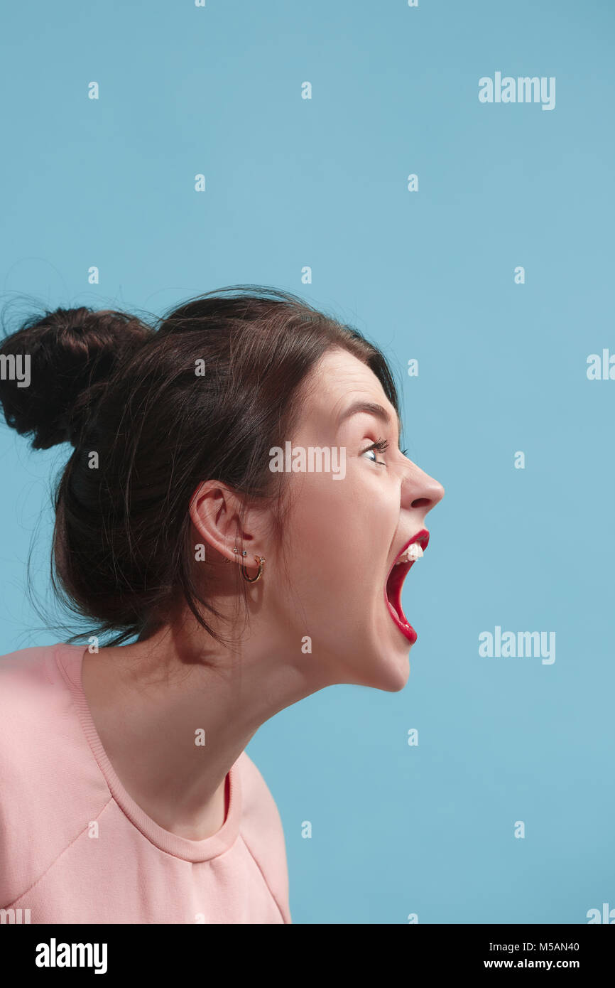 Il giovane arrabbiato emotiva donna urlando su blu di sfondo per studio Foto Stock