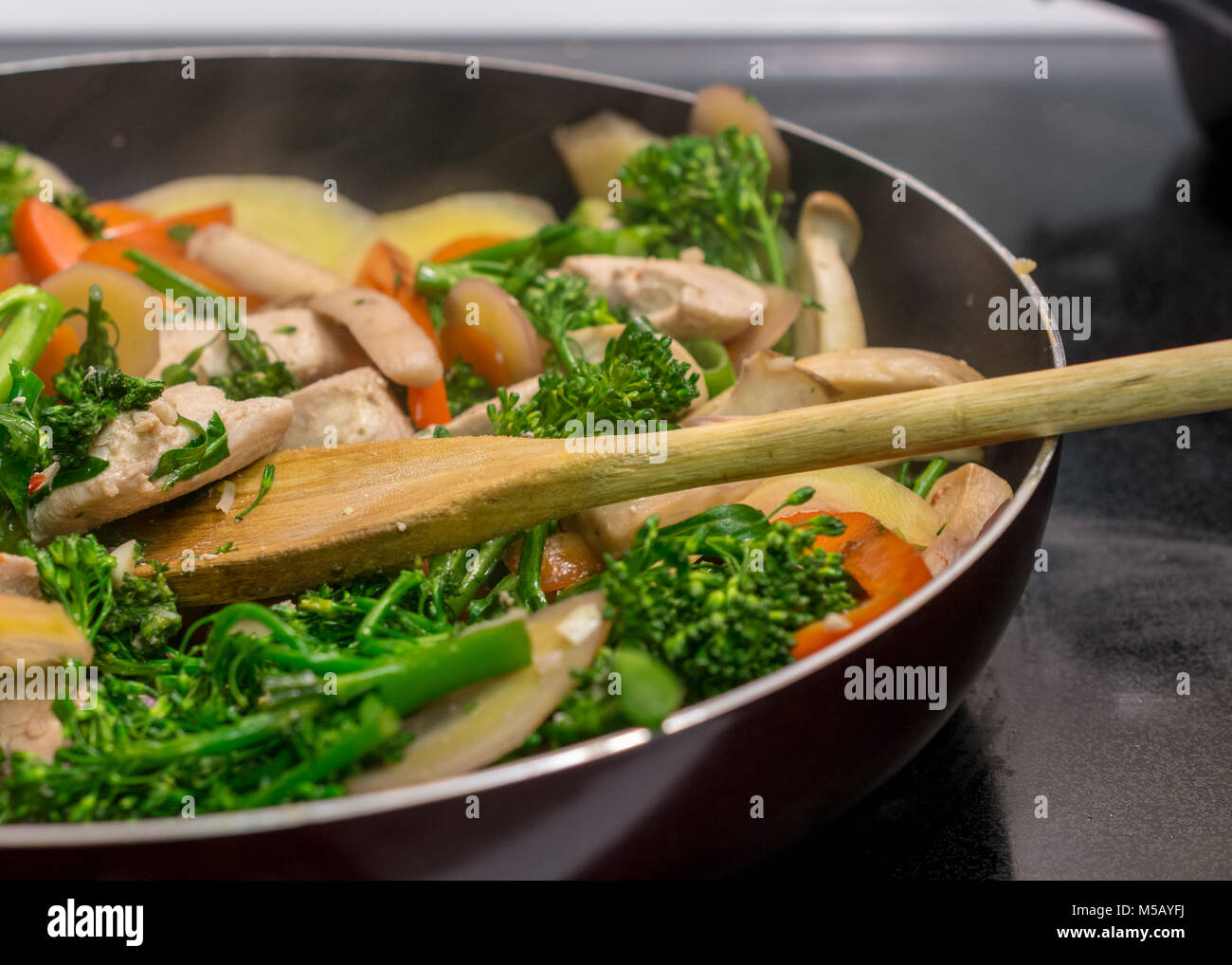 Close-up e vista laterale del cucchiaio di legno in agitazione il pollo e le verdure in padella in ghisa - mescolare la frittura Foto Stock