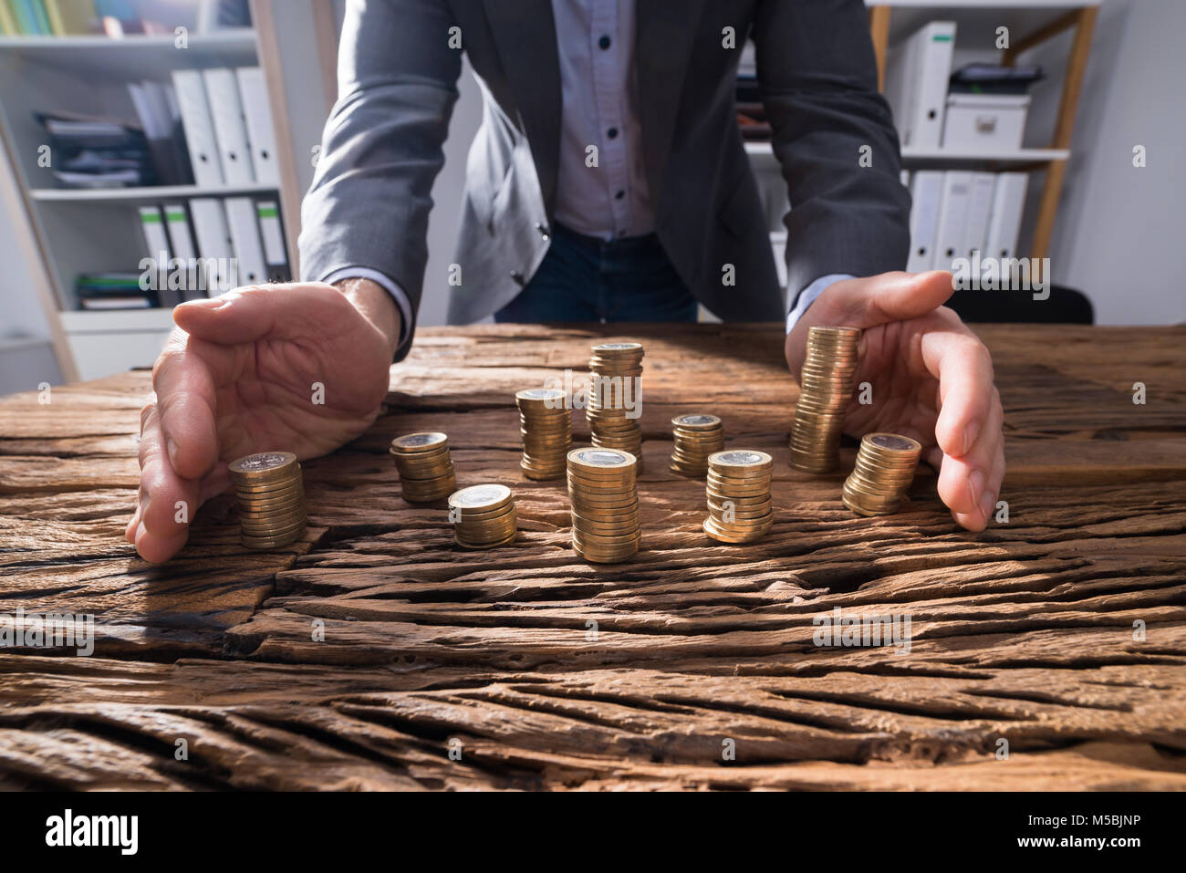 Commercianti la mano proteggere le monete impilate sulla scrivania in legno Foto Stock