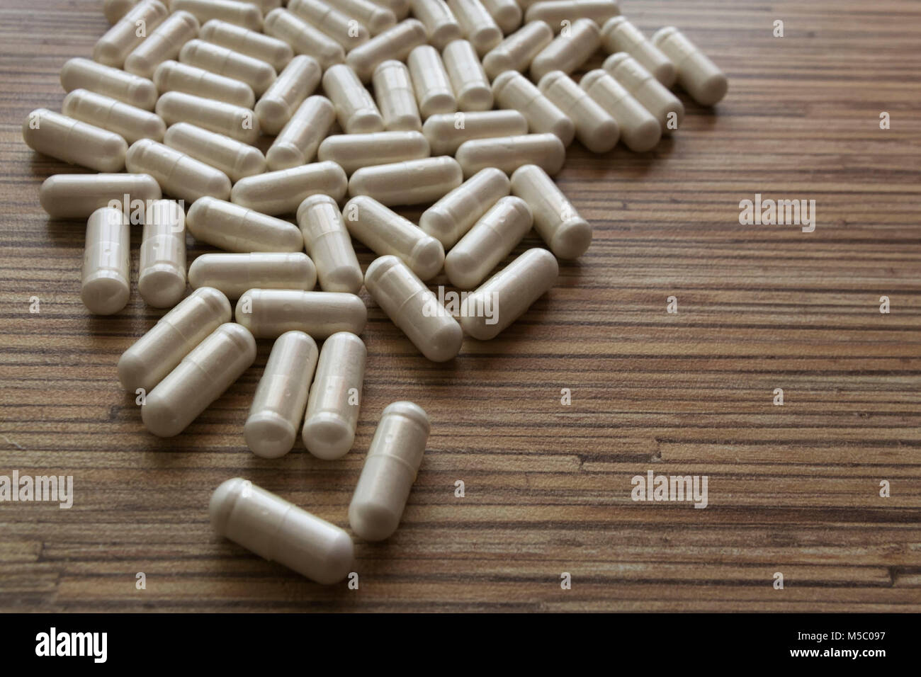 Pila di molti bianco ovale pillole di farmaco giacente in una pila sul tavolo di legno. Pila di pillole di bianco o di compresse Foto Stock