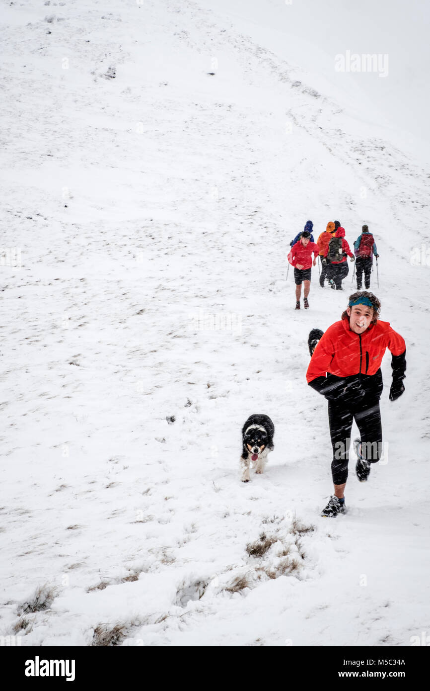 Allenamento di fitness in inverno. L'uomo con il suo cane in esecuzione nella neve, Kinder Scout, Derbyshire, Peak District, England, Regno Unito Foto Stock