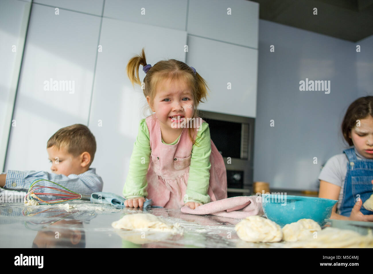 Tre bambini preparare qualcosa dall'impasto. Due sorelle e un fratello sono seduti al tavolo della cucina. Ci sono vari utensili di cucina sul Foto Stock