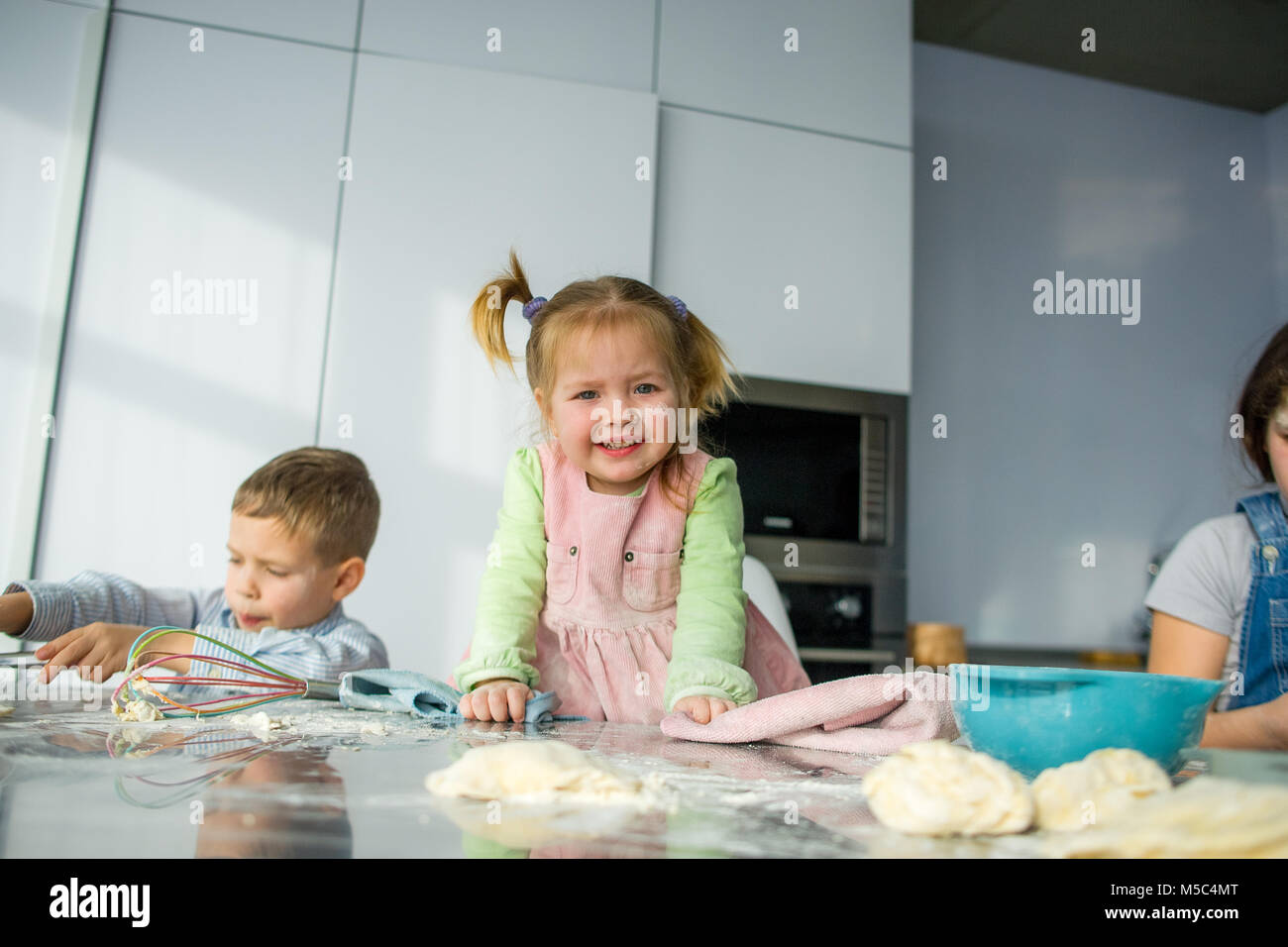 Tre bambini preparare qualcosa dall'impasto. Due sorelle e un fratello sono seduti al tavolo della cucina. Ci sono vari utensili di cucina sul Foto Stock