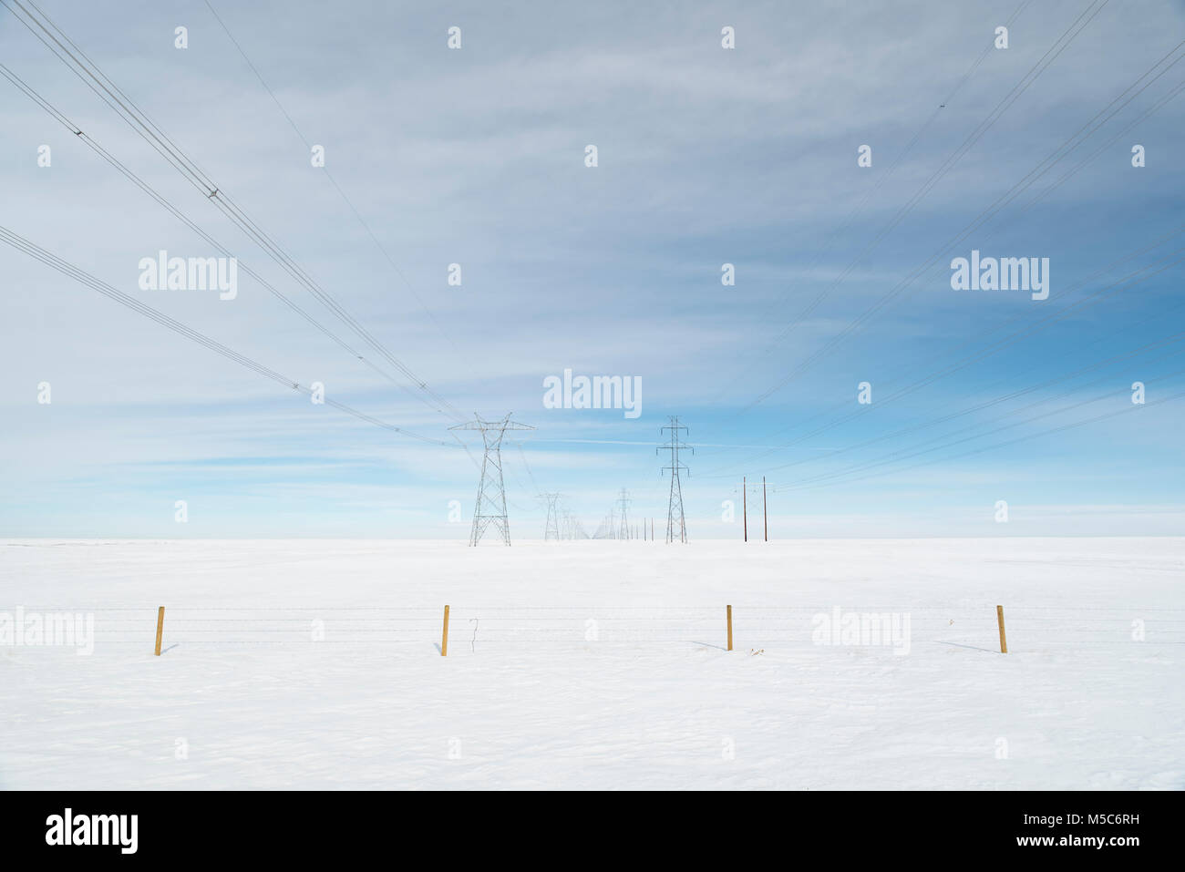 Alberta, Canada. Guardando verso il basso centro di a doppia fila di piloni di elettricità/torri di trasmissione sulle praterie d'inverno. Foto Stock