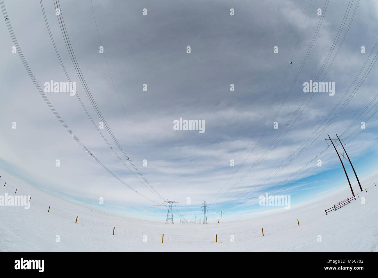 Alberta, Canada. Guardando verso il basso centro di a doppia fila di piloni di elettricità/torri di trasmissione sulle praterie in inverno, fisheye prospettiva. Foto Stock