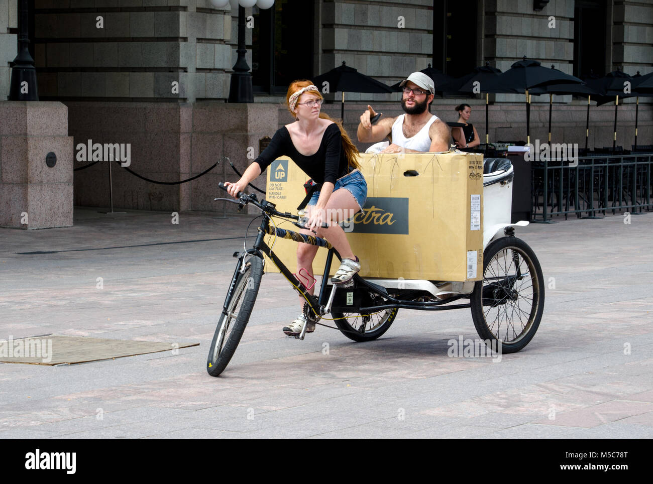 Agosto 4, 2014; i mezzi di trasporto pubblici va verde a Denver CO come una femmina bike taxi prende il suo passeggero e del suo grande ne w TV home. Foto Stock