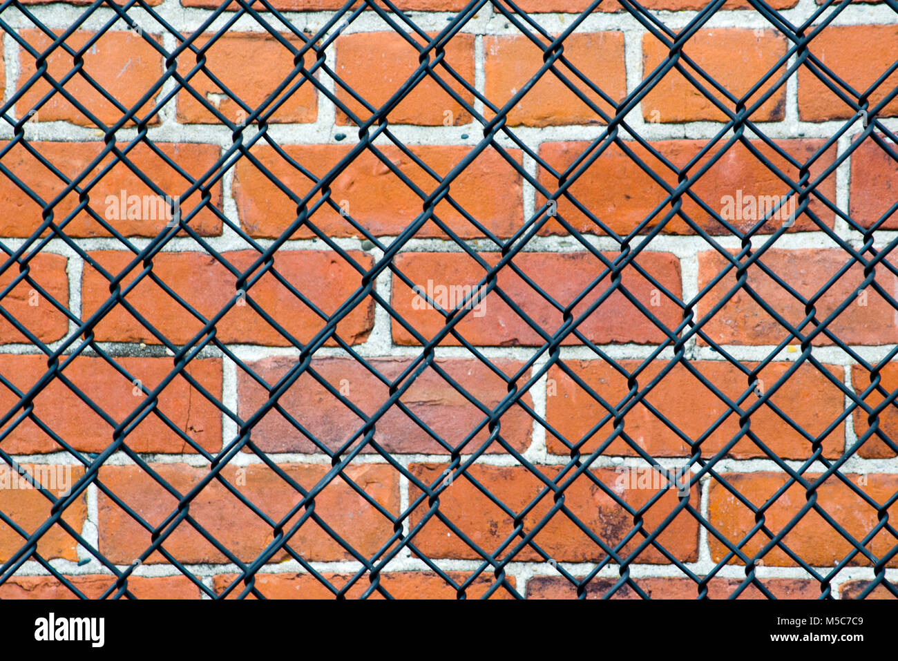 Muro di mattoni dietro una catena collegamento recinto. Ciò significa tenere fuori o è qualcosa destinato ad essere mantenuto in? Foto Stock