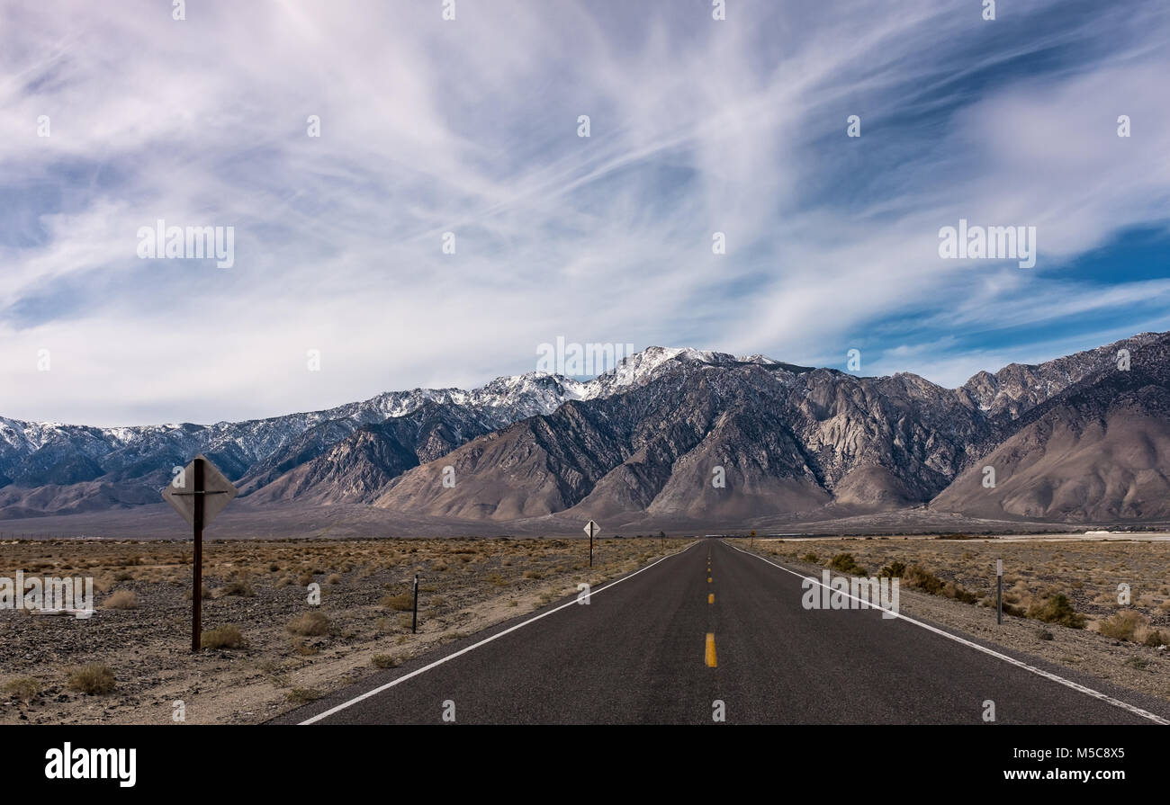 Infinito Vuoto diritta autostrada nel deserto con la gamma della montagna in background e drammatici nuvoloso cielo blu. Strada viaggio attraverso la Valle della Morte in California Foto Stock