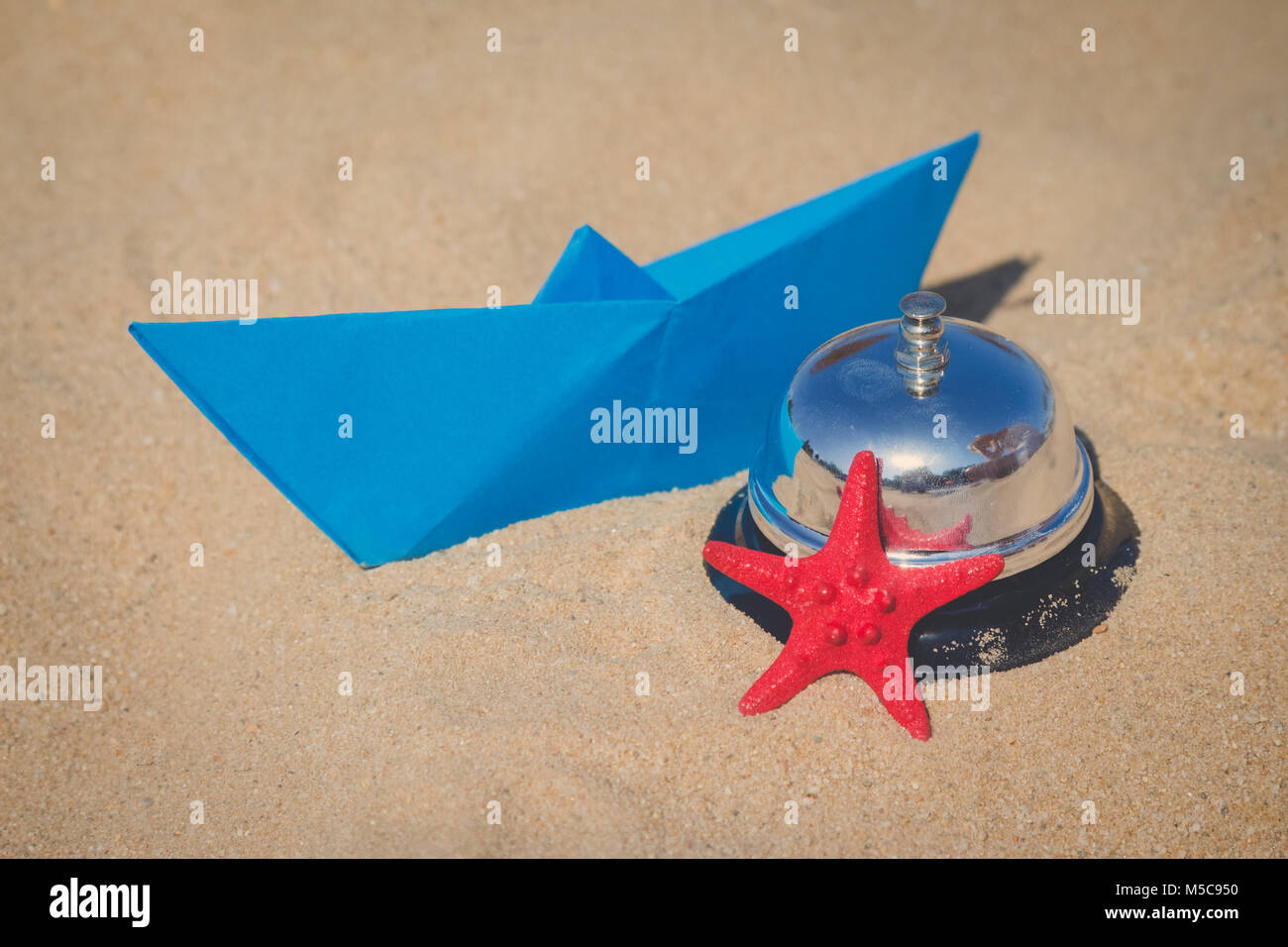 Estate oggetti concetto. Barca di carta, stella di mare e il servizio campana sulla spiaggia sabbiosa Foto Stock