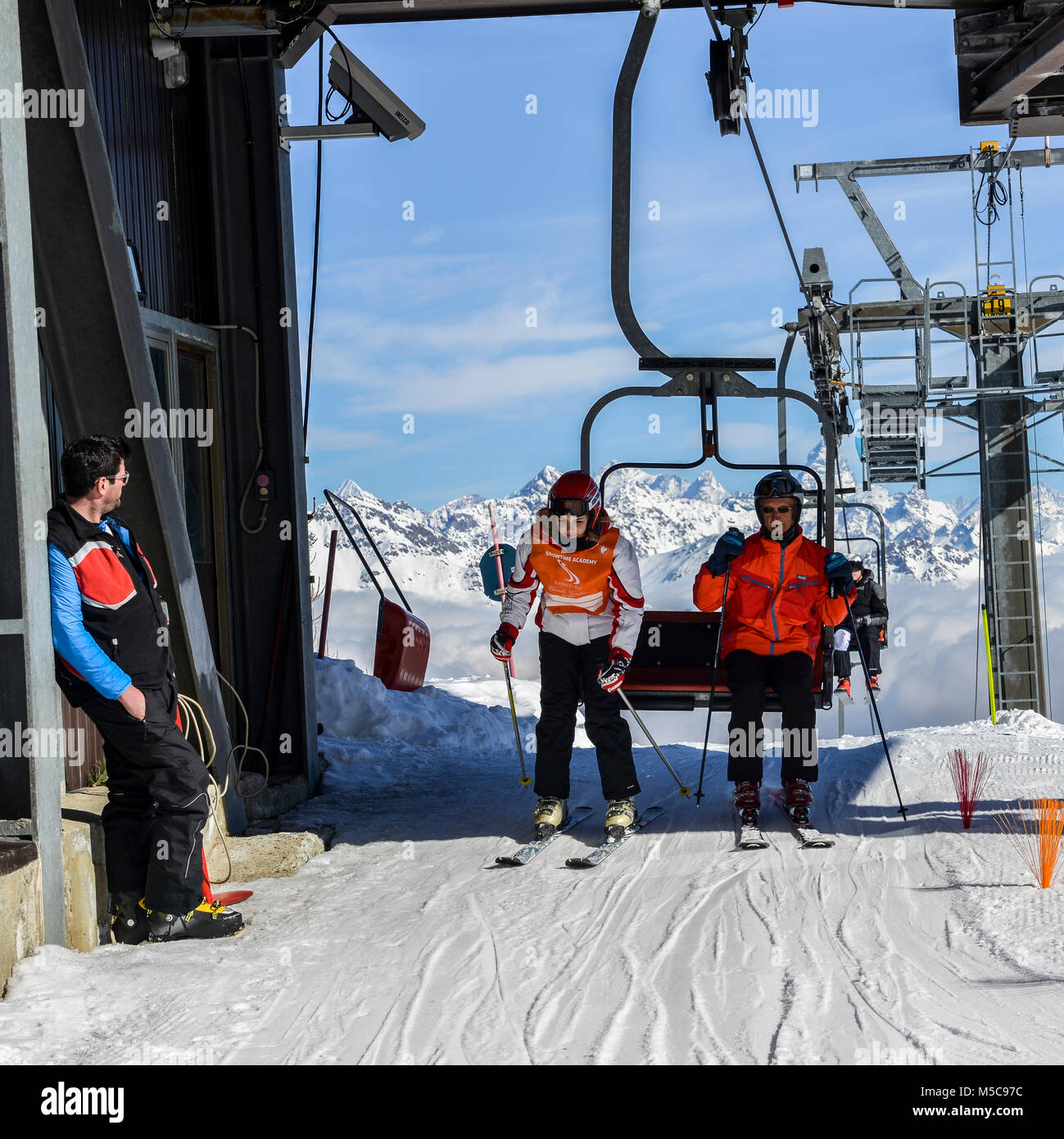 Pila, Aosta, Italia - 19 Feb 2018: uomo più anziano e adolescente scendere seggiovia alla stazione sciistica con le maestose Alpi Italiane in background Foto Stock