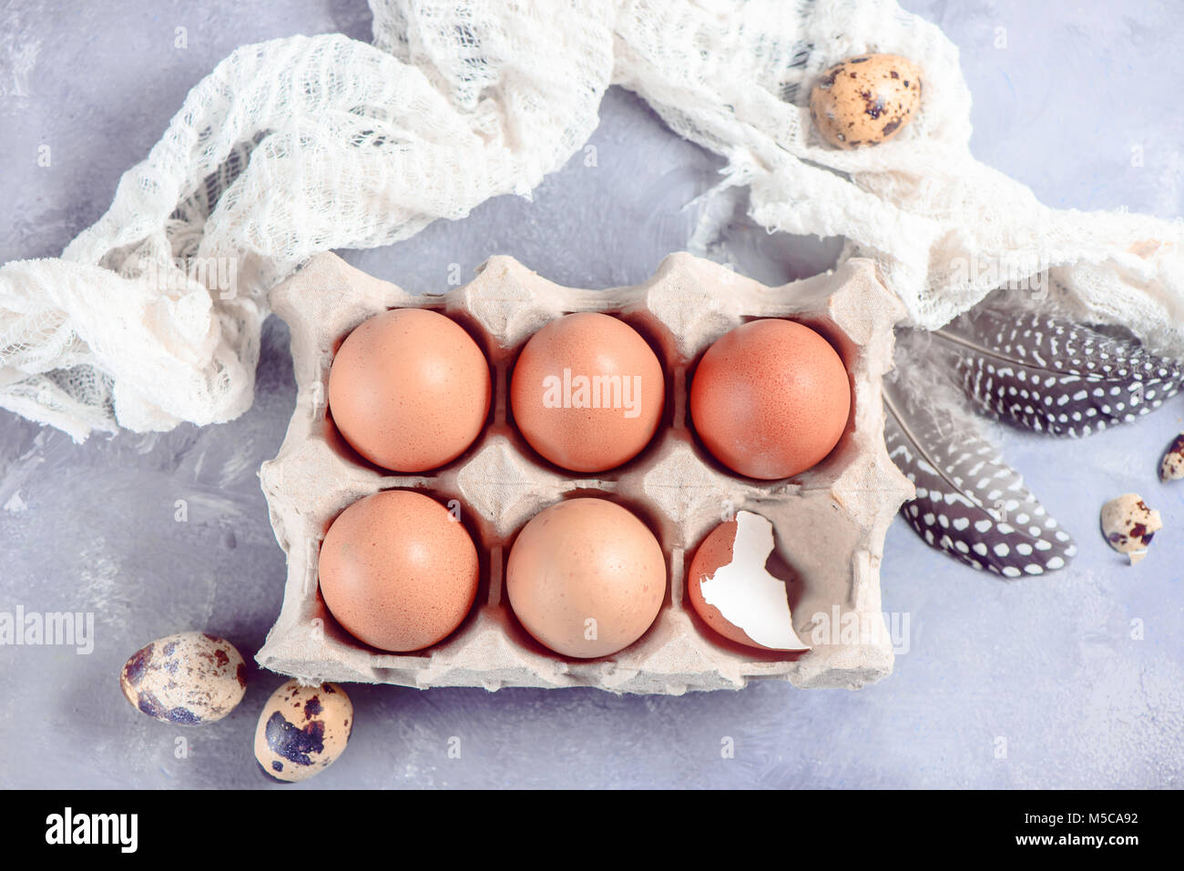 Fresco uova marrone nel mestiere del vassoio della carta su uno sfondo luminoso con piume e panno. Ingredienti per la cottura di Pasqua. Tasto alto testata con copia spazio. Foto Stock