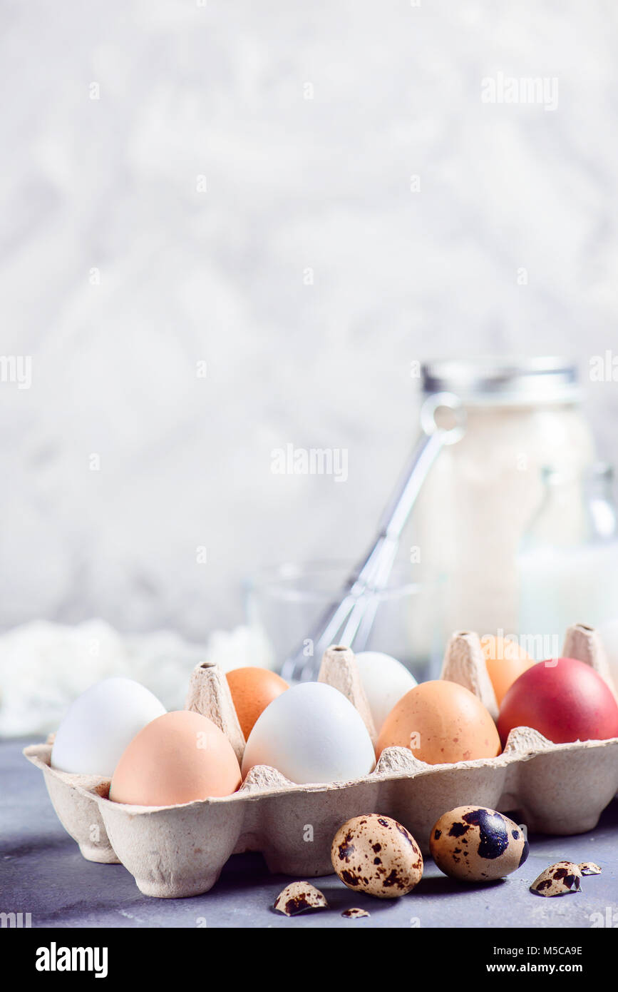 Fresca bruna e le uova bianche nel mestiere del vassoio della carta su uno sfondo luminoso con uova di quaglia, frusta e gli ingredienti per la cottura di Pasqua. Tasto alto background wi Foto Stock