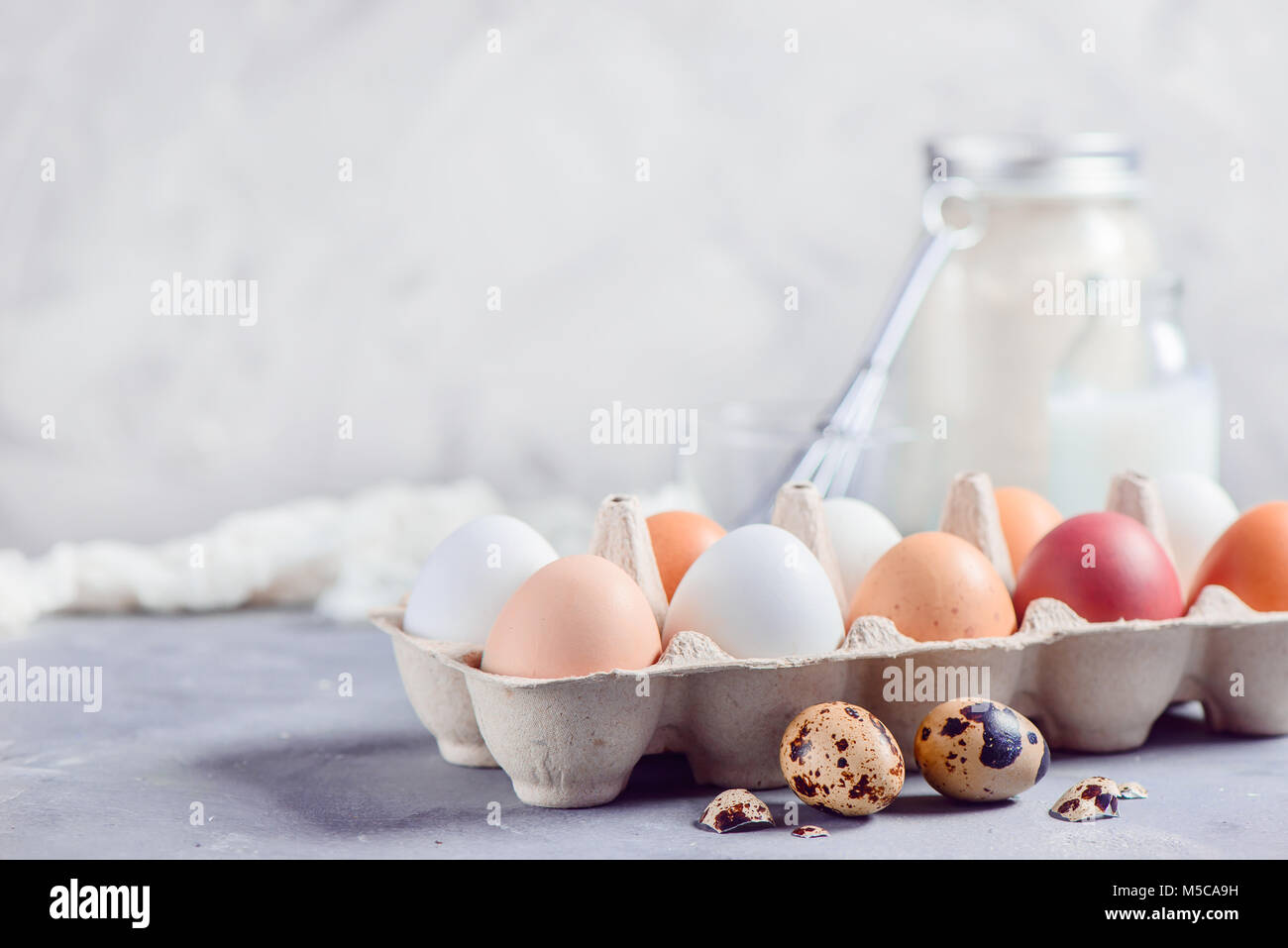 Fresca bruna e le uova bianche nel mestiere del vassoio della carta su uno sfondo luminoso con uova di quaglia, frusta e gli ingredienti per la cottura di Pasqua. Tasto alto background wi Foto Stock