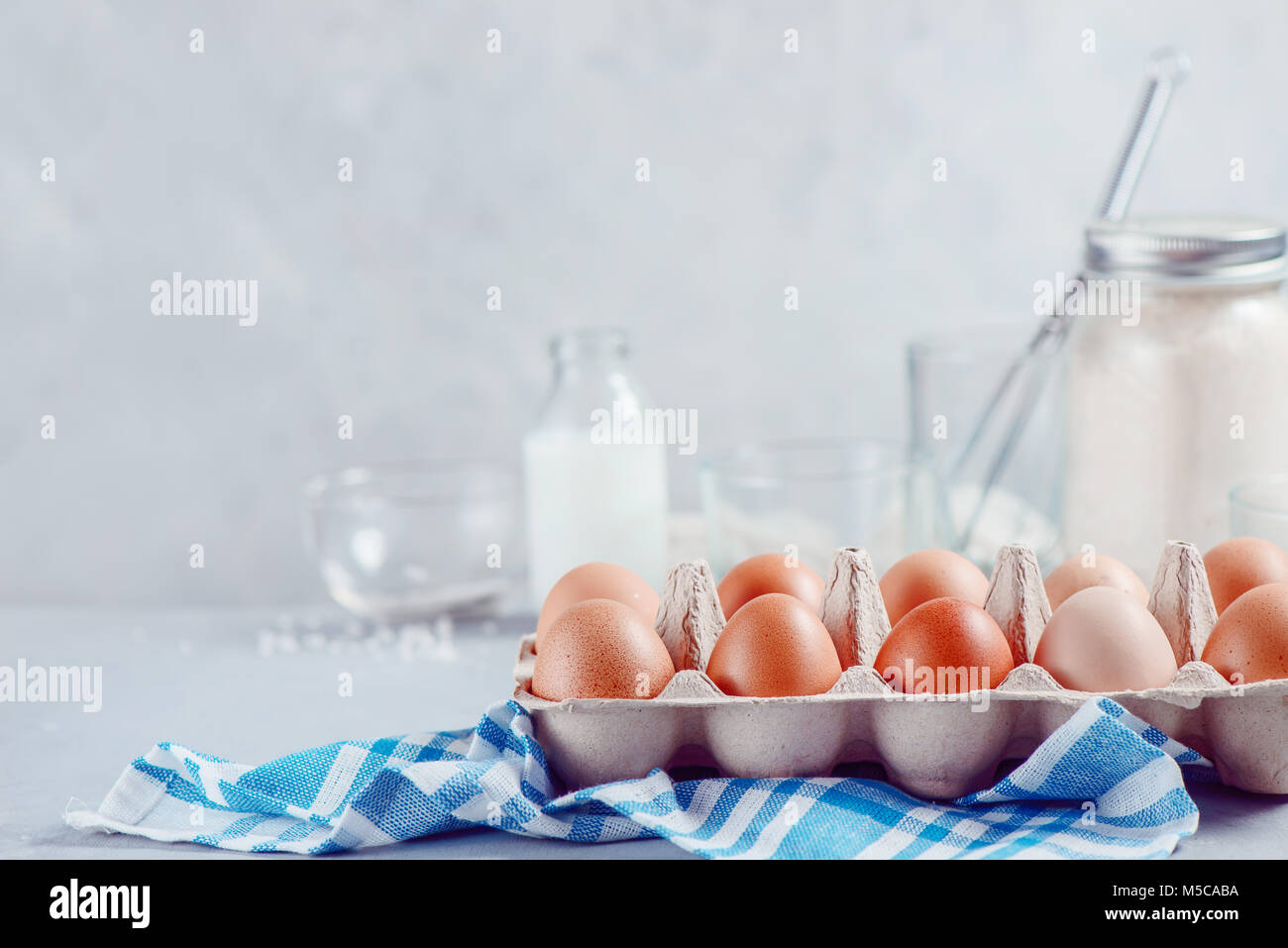Le uova in un vassoio della carta su uno sfondo luminoso con il latte, la farina e gli ingredienti per la cottura di Pasqua. Elevato La chiave dello sfondo con copia spazio. Foto Stock
