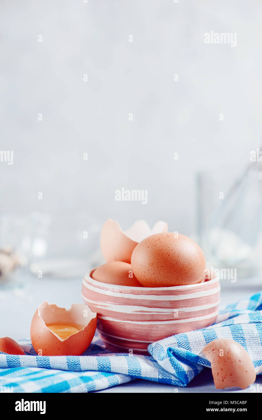 Rosolare le uova in un recipiente di ceramica su uno sfondo luminoso con il latte, la farina e gli ingredienti per la cottura di Pasqua. Elevato La chiave dello sfondo con copia spazio. Foto Stock