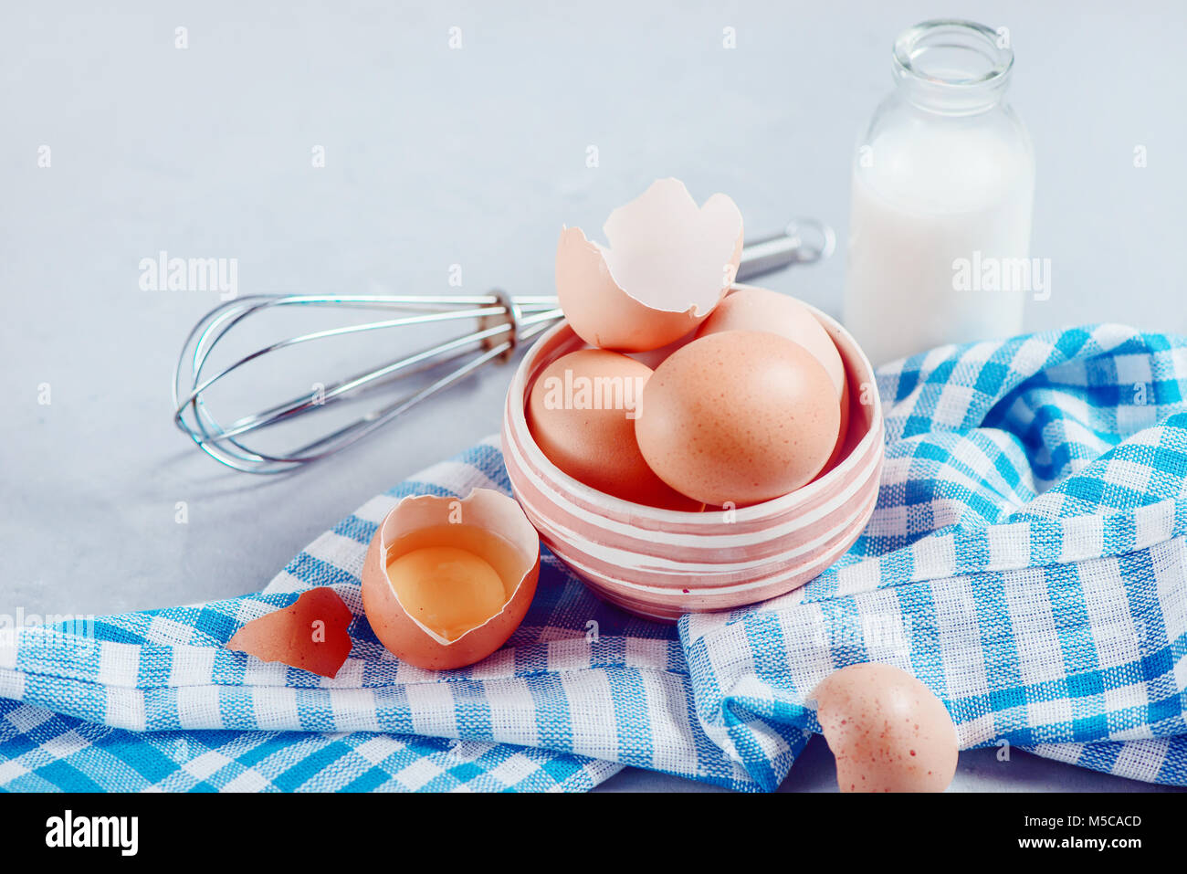 Rosolare le uova in un recipiente di ceramica su uno sfondo luminoso con il latte, la farina e gli ingredienti per la cottura di Pasqua. Elevato La chiave dello sfondo con copia spazio. Foto Stock