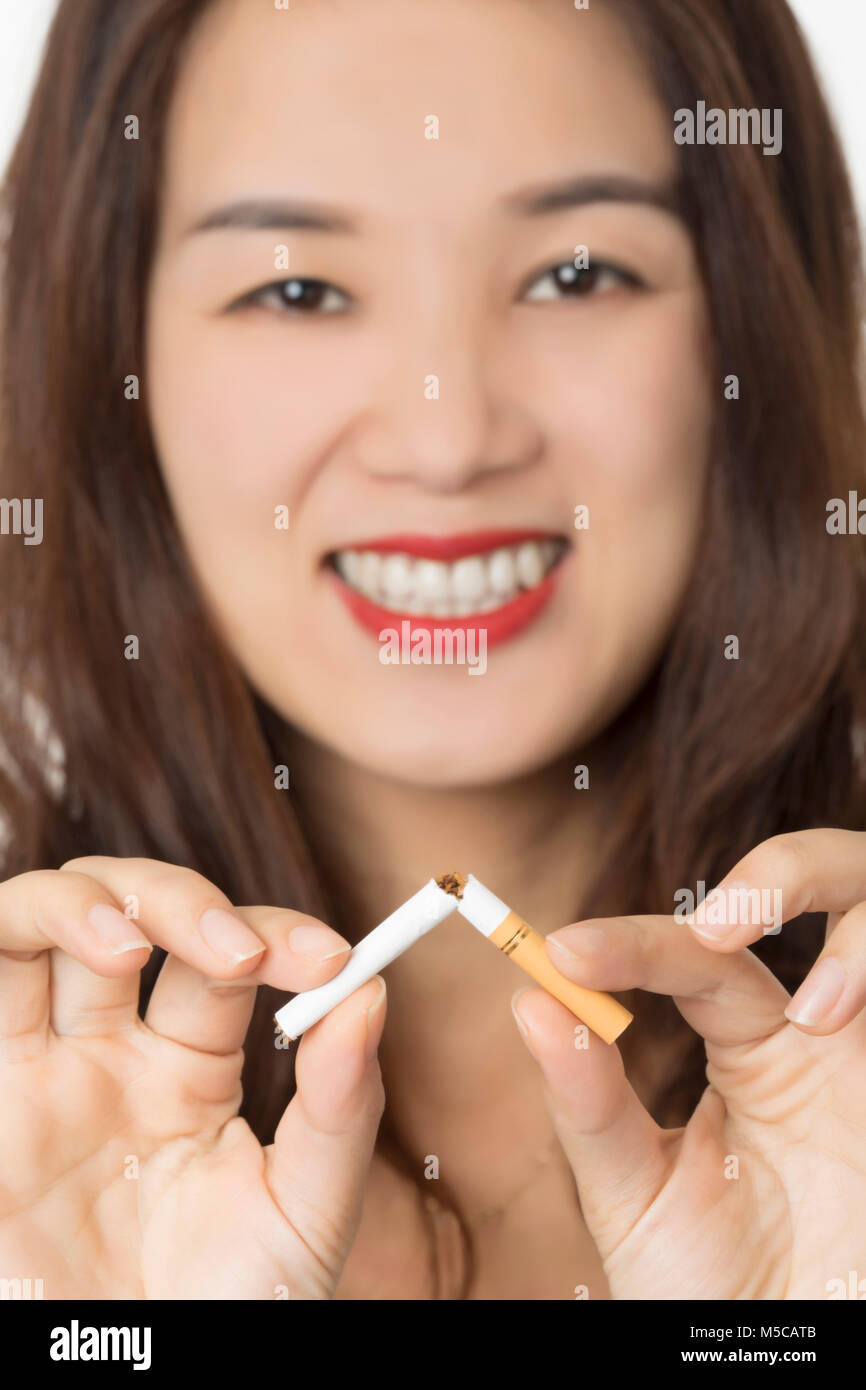 Bella donna asiatica sorridere mentre la rottura di una sigaretta per smettere di fumare isolato su uno sfondo bianco Foto Stock