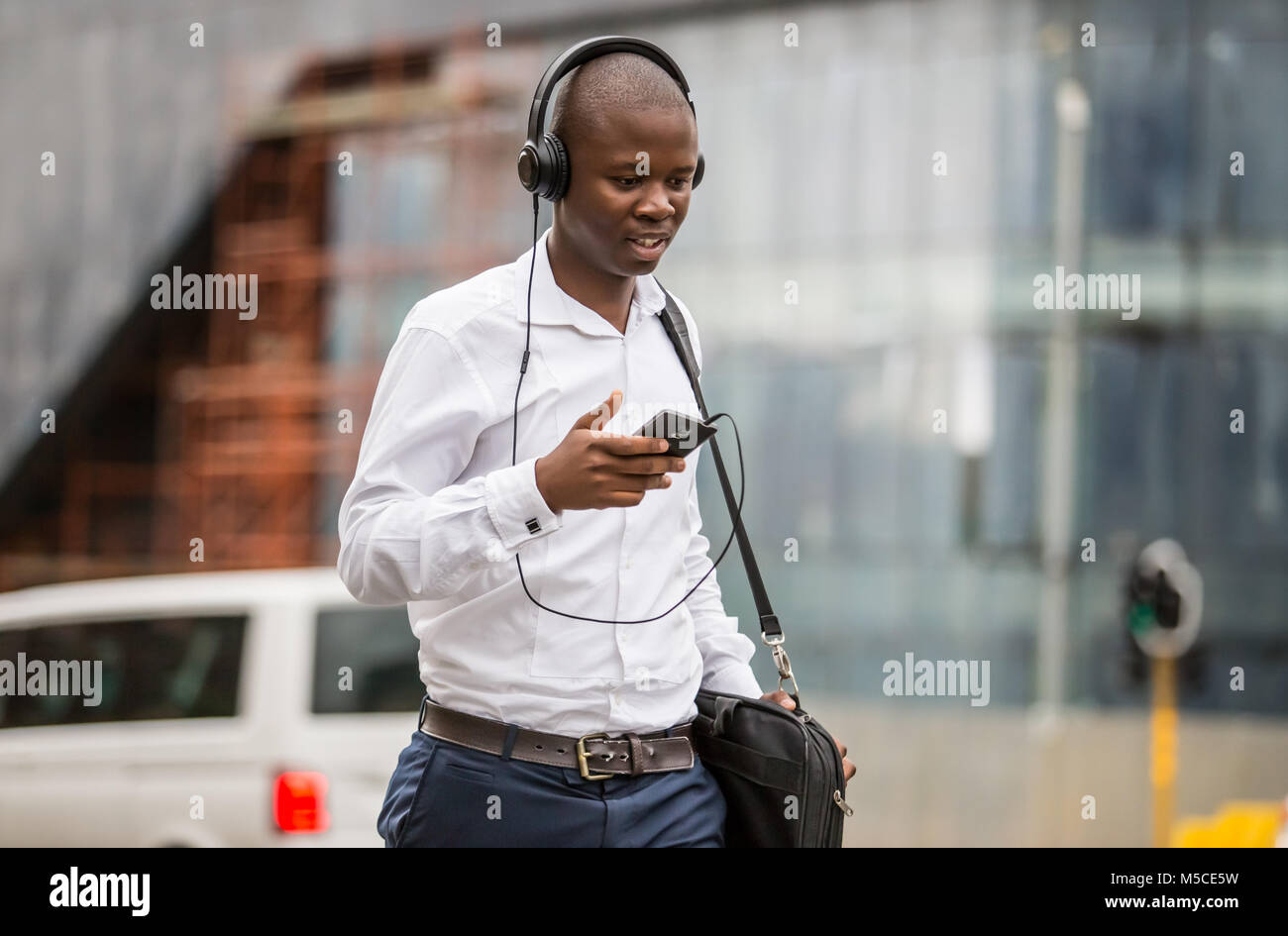 L'uomo camminare per strada con le cuffie e il telefono cellulare in mano. Johannesburg, Sud Africa - 15 Febbraio 2018 Foto Stock