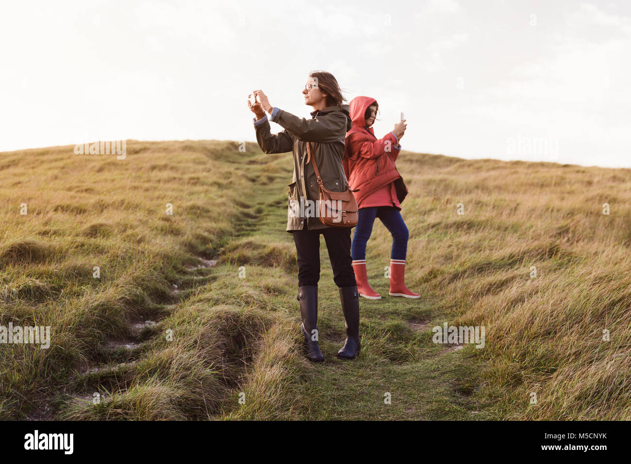 Madre e figlia godendo di una splendida vista, utilizzare smart phone per scattare delle foto su una verde collina, autunno escursionismo in Inghilterra. Foto Stock