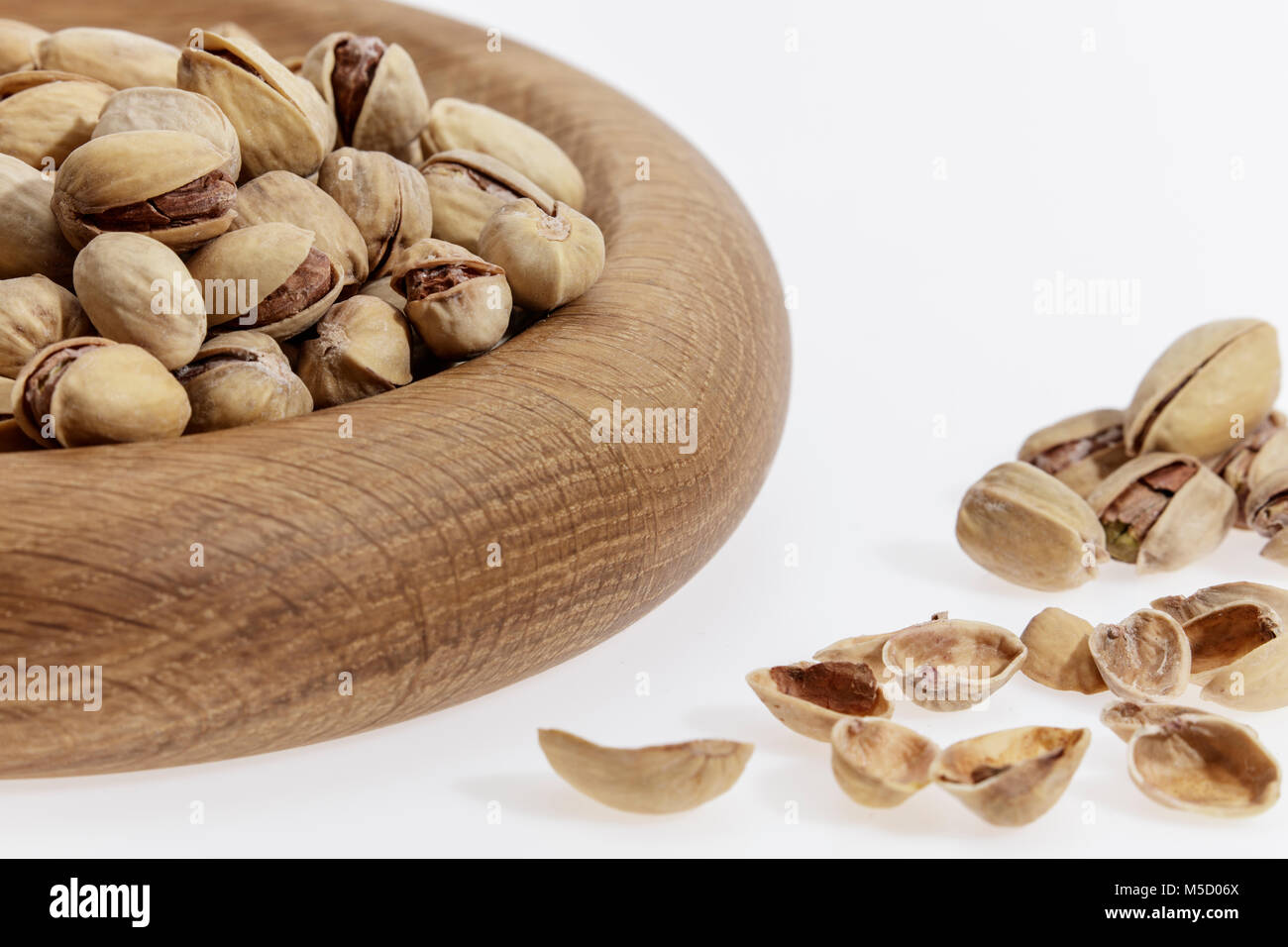 I pistacchi e conchiglie in una ciotola di legno contro un pulito lo sfondo bianco Foto Stock