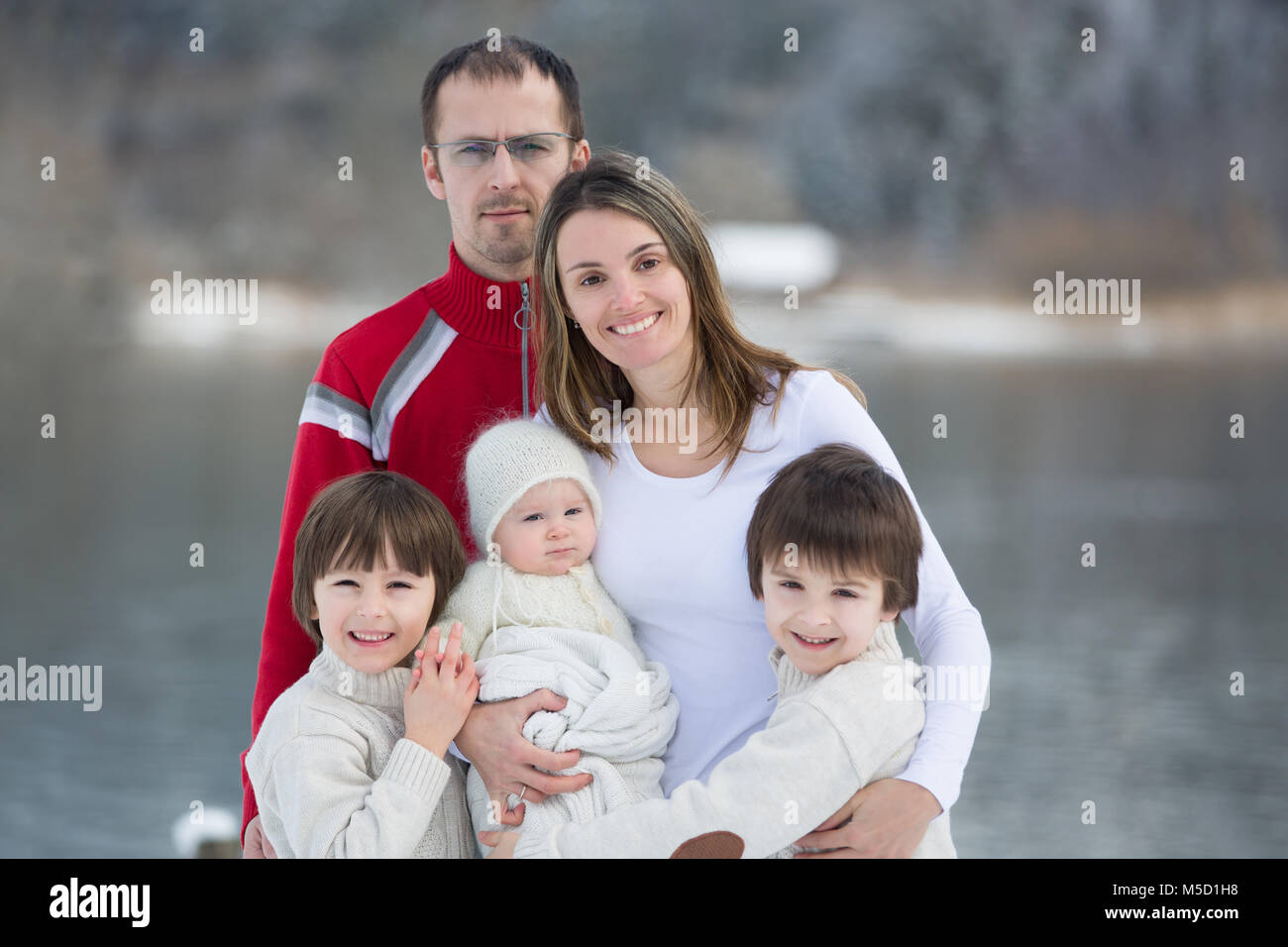 La famiglia felice, madre, padre e tre bambini avente ritratto di famiglia su un soleggiato inverno nevoso di giorno in un lago in Austria, il paesaggio paesaggio Foto Stock