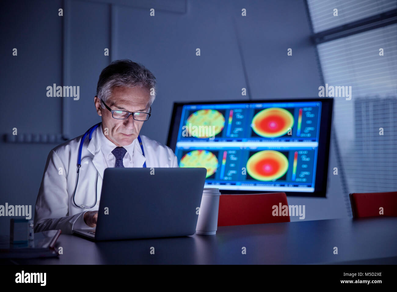 Focalizzato chirurgo maschio lavora al computer portatile in ospedale Foto Stock