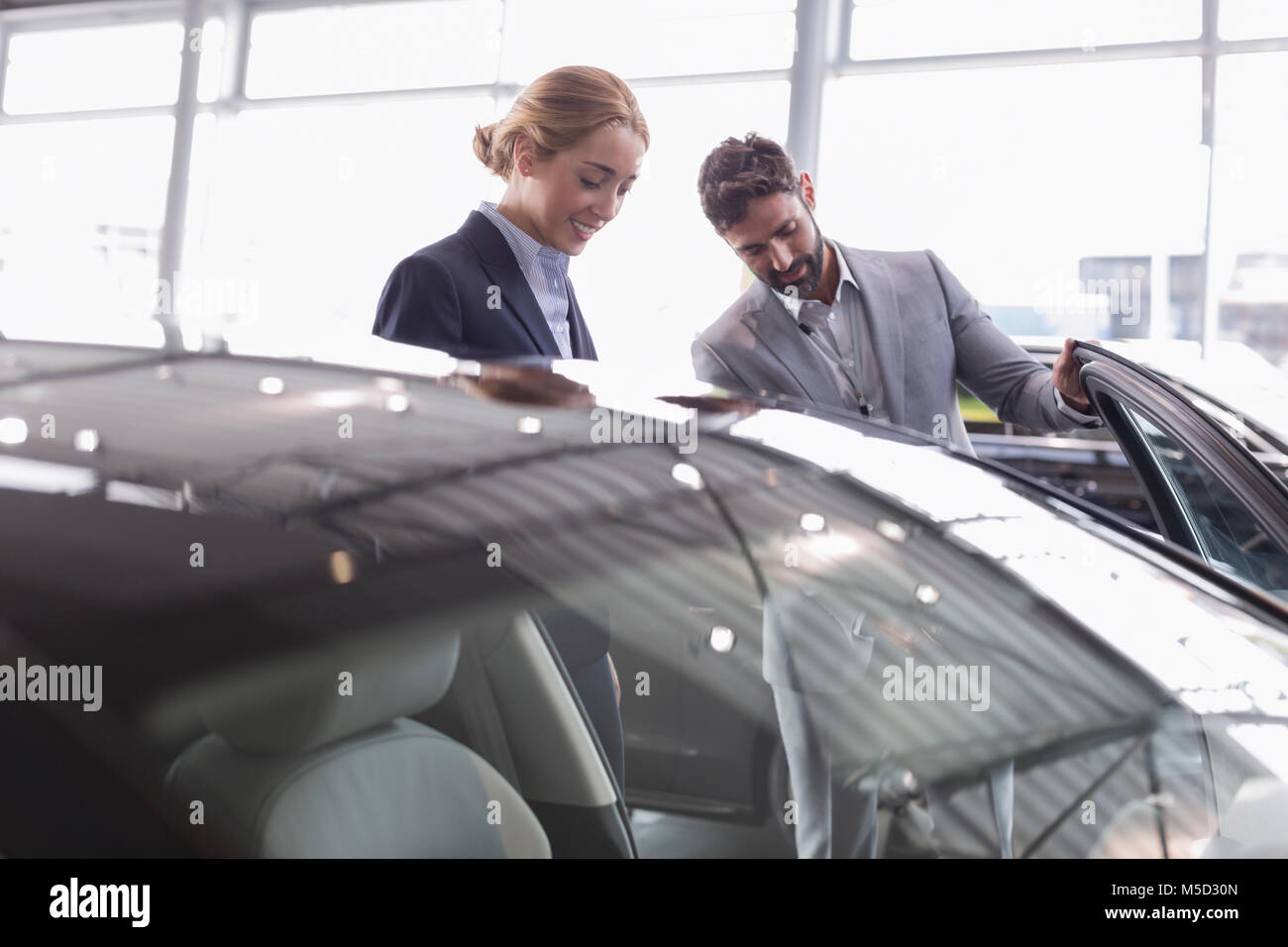 Venditore auto che mostra la nuova auto per i clienti di sesso femminile in concessionaria auto showroom Foto Stock