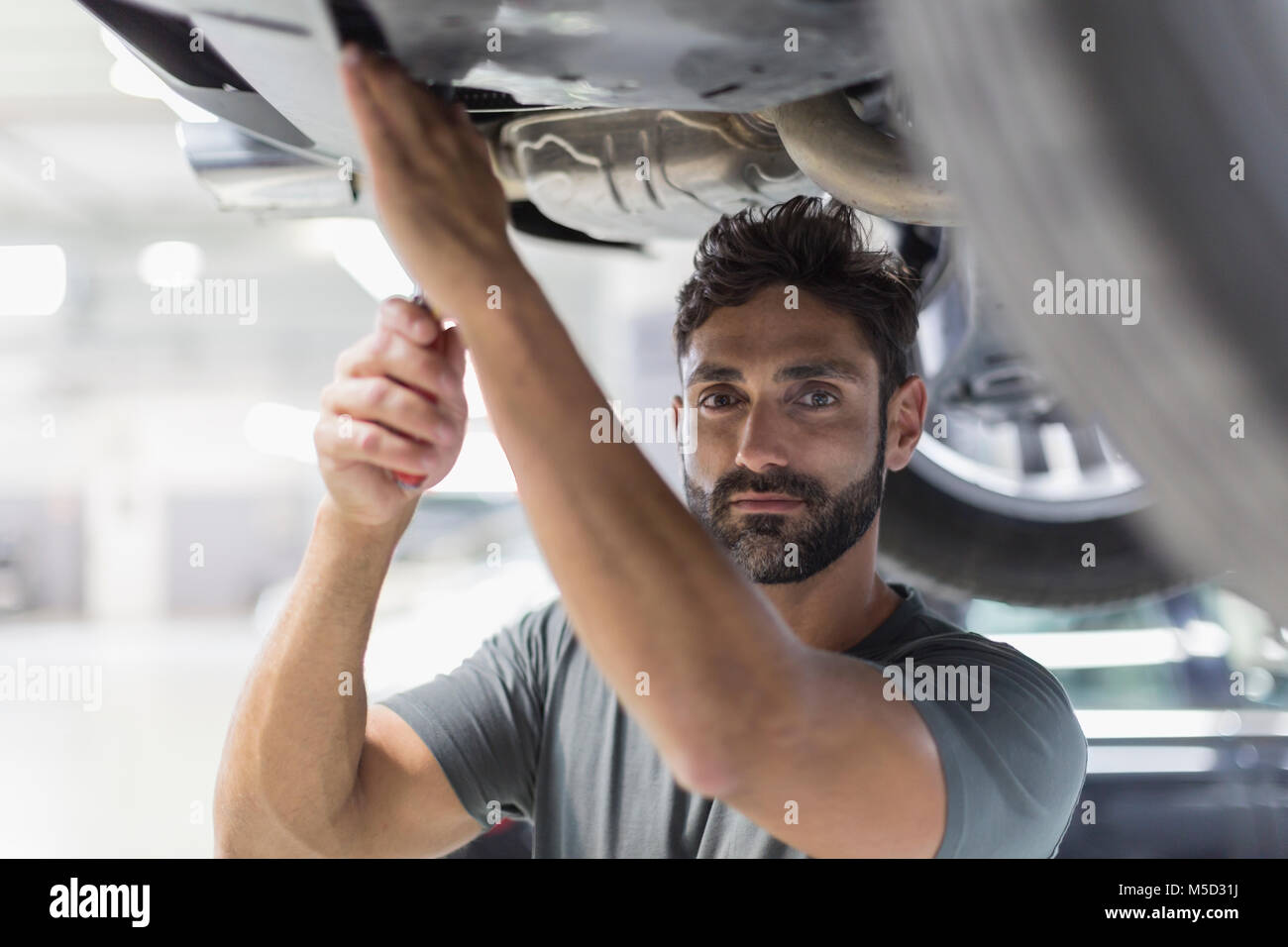 Ritratto maschile serio lavoro meccanico sotto auto nel negozio di riparazioni auto Foto Stock