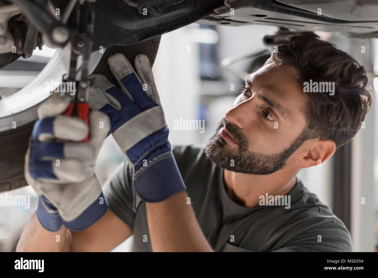 Concentrato maschio fissaggio meccanico al di sotto della ruota auto nel negozio di riparazioni auto Foto Stock