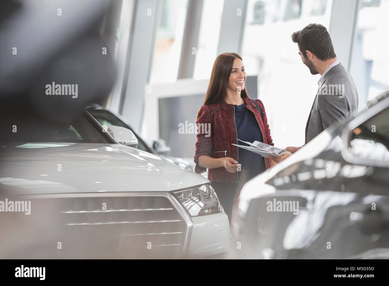 Commessa per auto che mostra la brochure al cliente maschio in concessionaria auto showroom Foto Stock