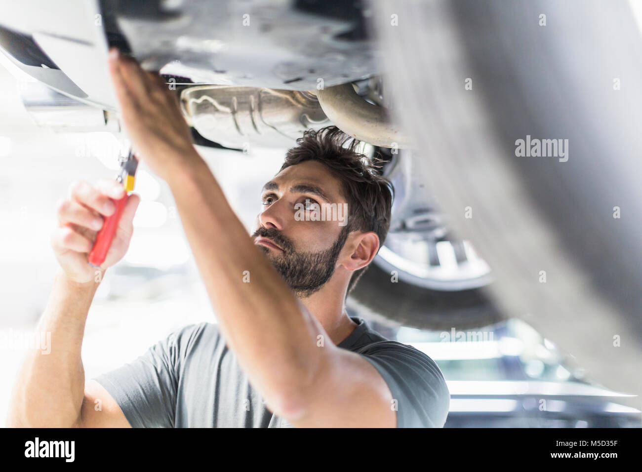 Focalizzato meccanico maschio lavora sotto auto nel negozio di riparazioni auto Foto Stock
