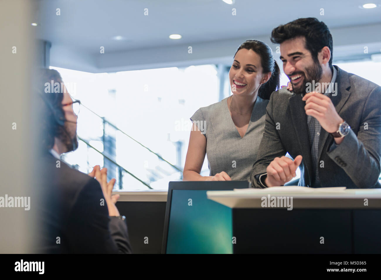 Coppia sorridente i clienti parlando di receptionist al desk in concessionaria auto Foto Stock