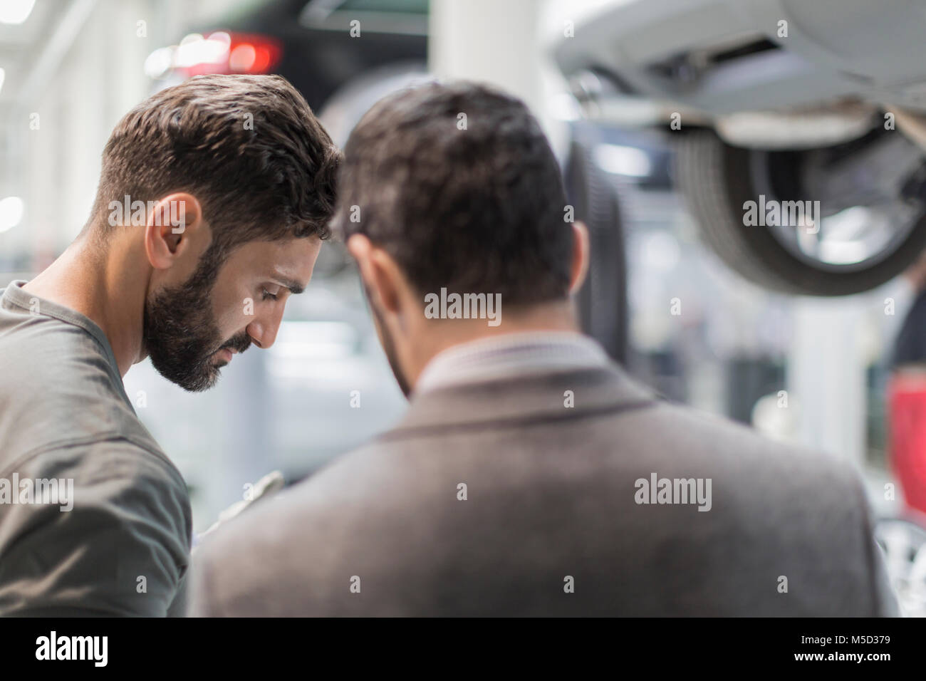 Meccanico maschio e il cliente a parlare, guardando verso il basso nel negozio di riparazioni auto Foto Stock