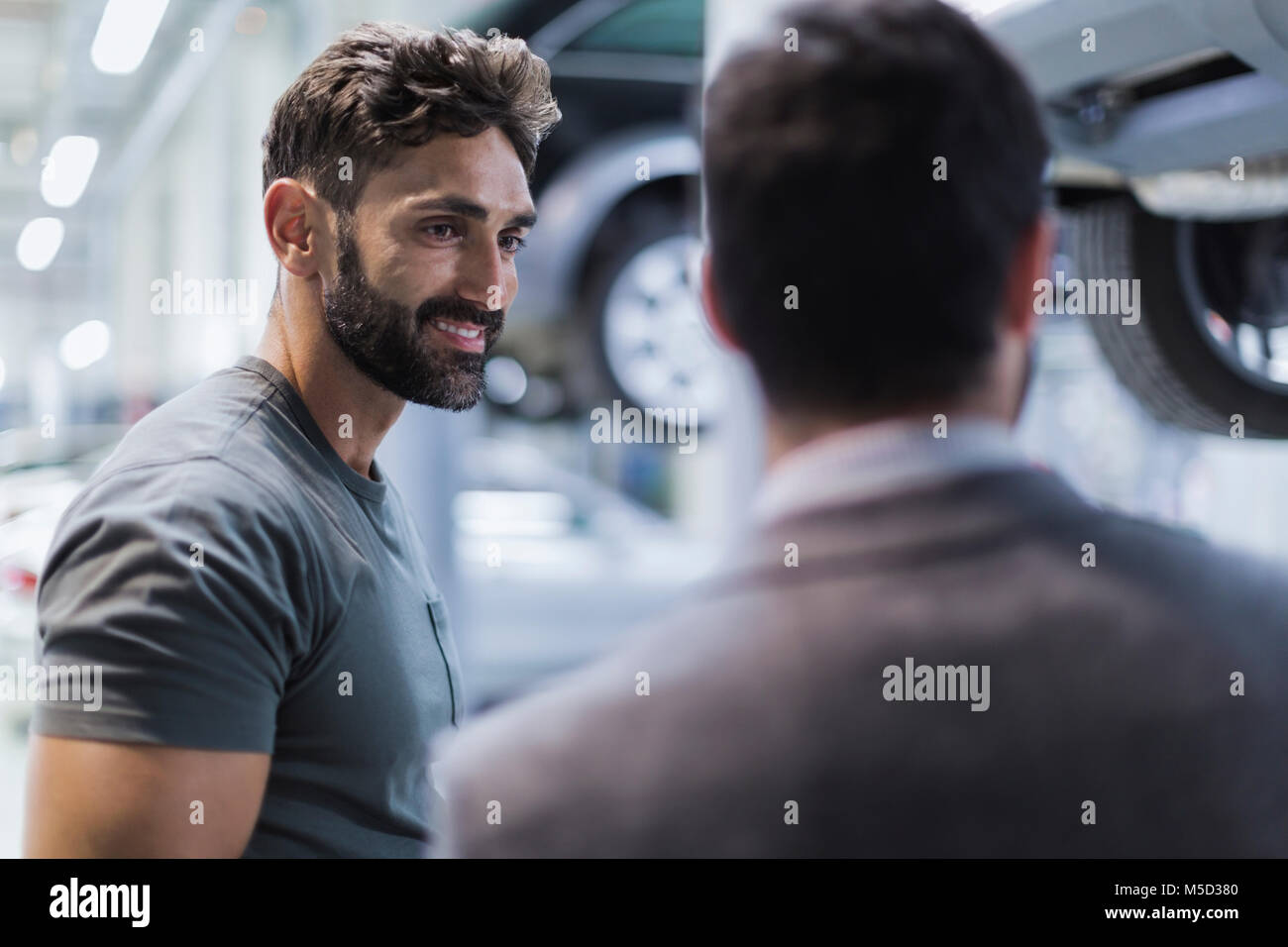 Sorridente maschio meccanico automatico a parlare con il cliente in negozio di riparazioni auto Foto Stock