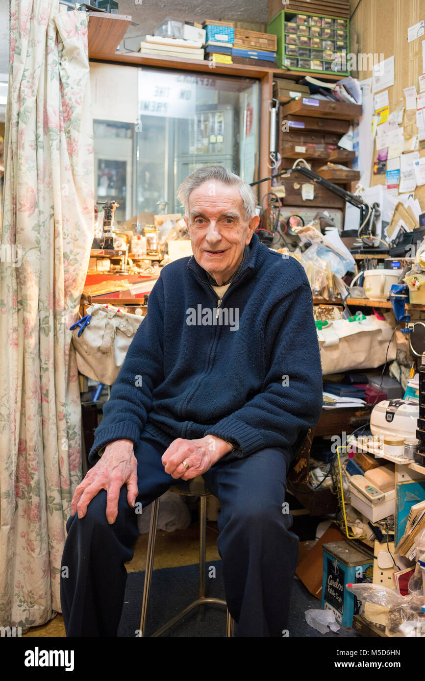 Un vecchio sperimentato riparazione orologi uomo si siede nel suo negozio al suo banco da lavoro Foto Stock