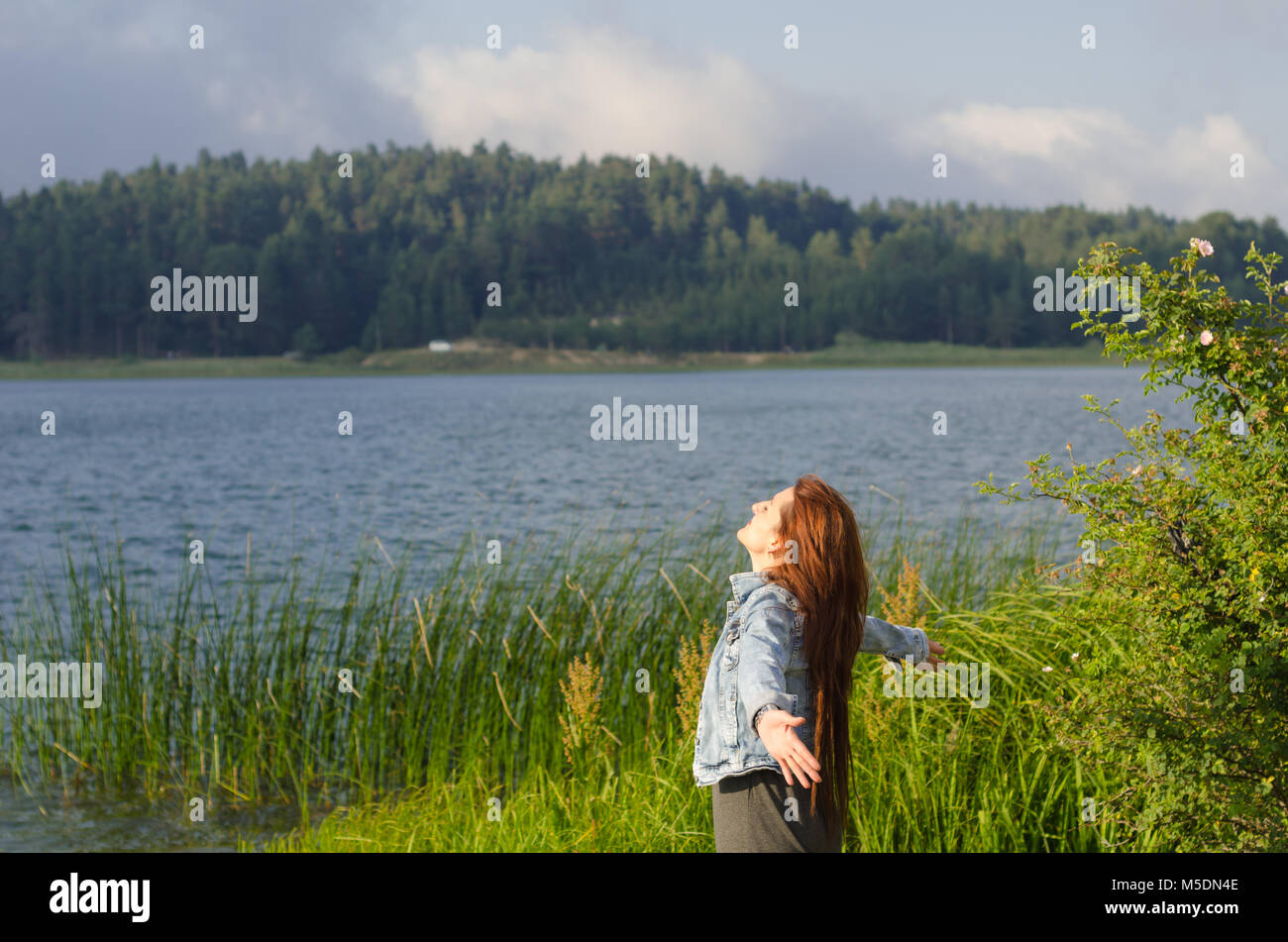 Ha aperto le sue braccia sulla riva del lago e voltò la faccia verso il vento, un solitario giovane donna, Foto Stock