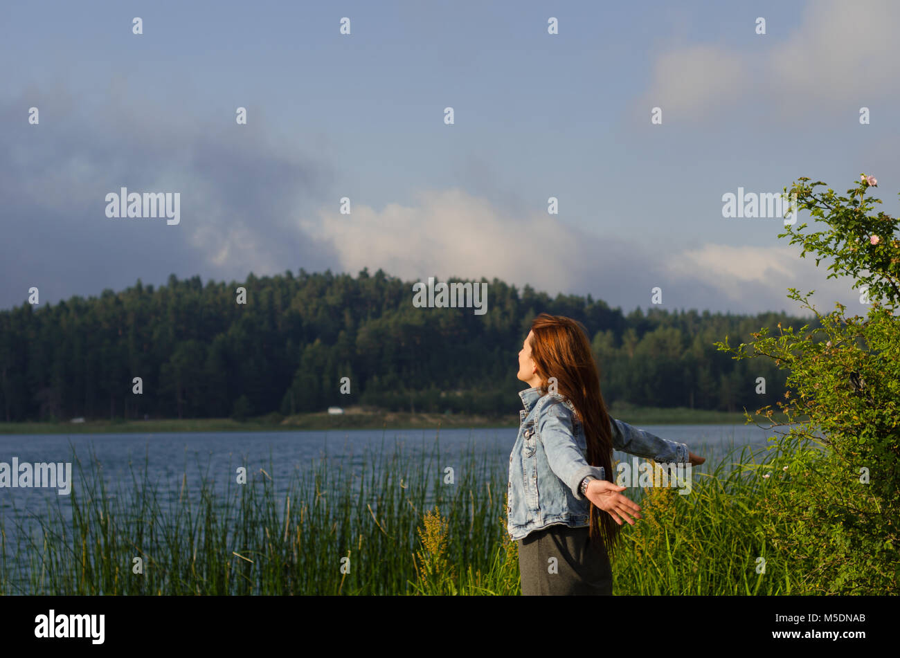 Ha aperto le sue braccia sulla riva del lago e voltò la faccia verso il vento, un solitario giovane donna, Foto Stock