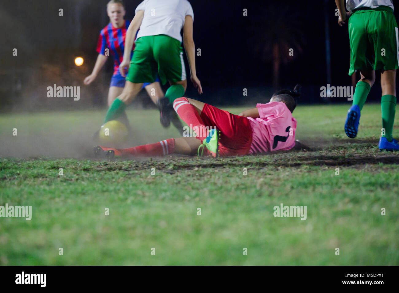 Femmina giovane giocatore di calcio cade, calciare il pallone che giocano a calcio sul campo di notte Foto Stock