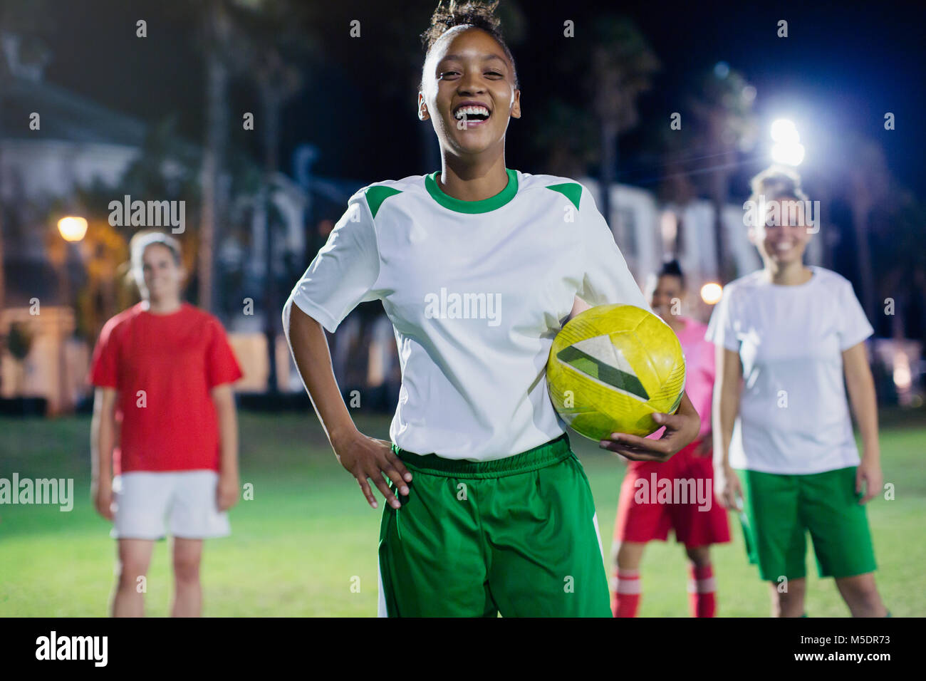 Ritratto fiduciosi, ridendo femmina giovane giocatore di calcio la pratica sul campo di notte Foto Stock