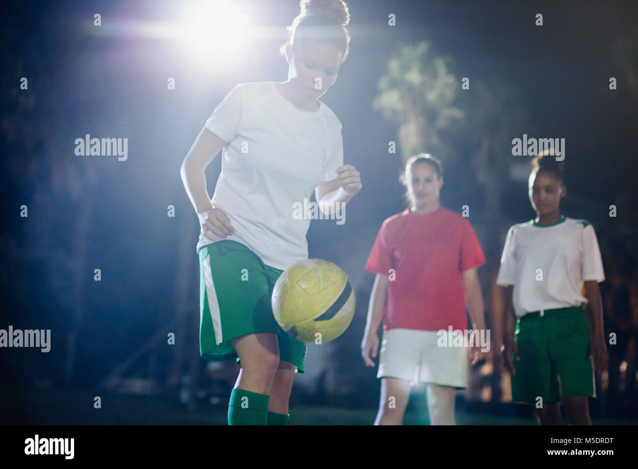 Focalizzato femmina giovane giocatore di calcio la pratica sul campo di notte, kneeing la sfera Foto Stock