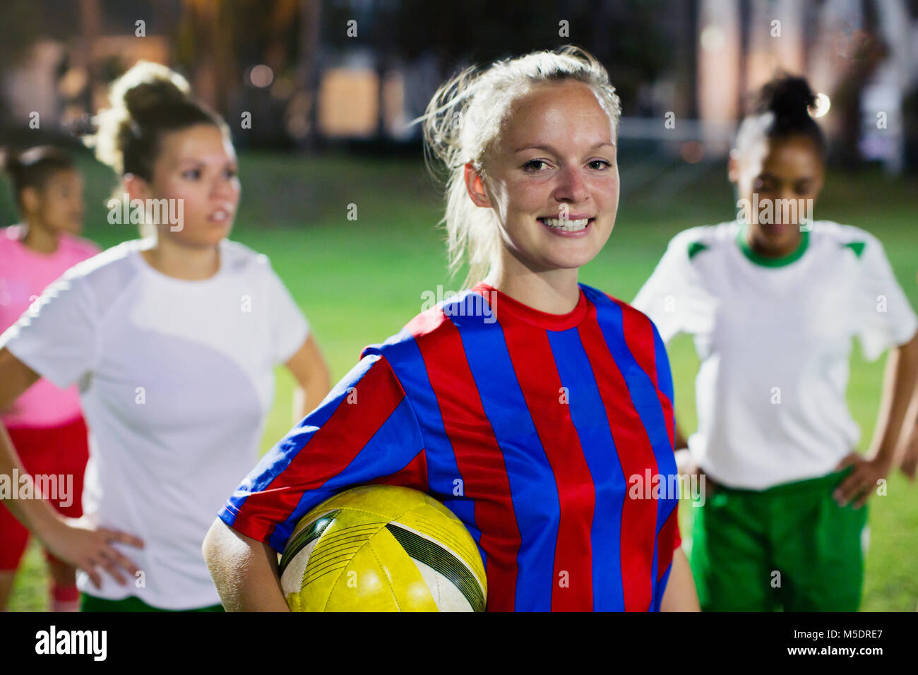 Ritratto sorridente e fiducioso femmina giovane giocatore di calcio con la palla sul campo di notte Foto Stock