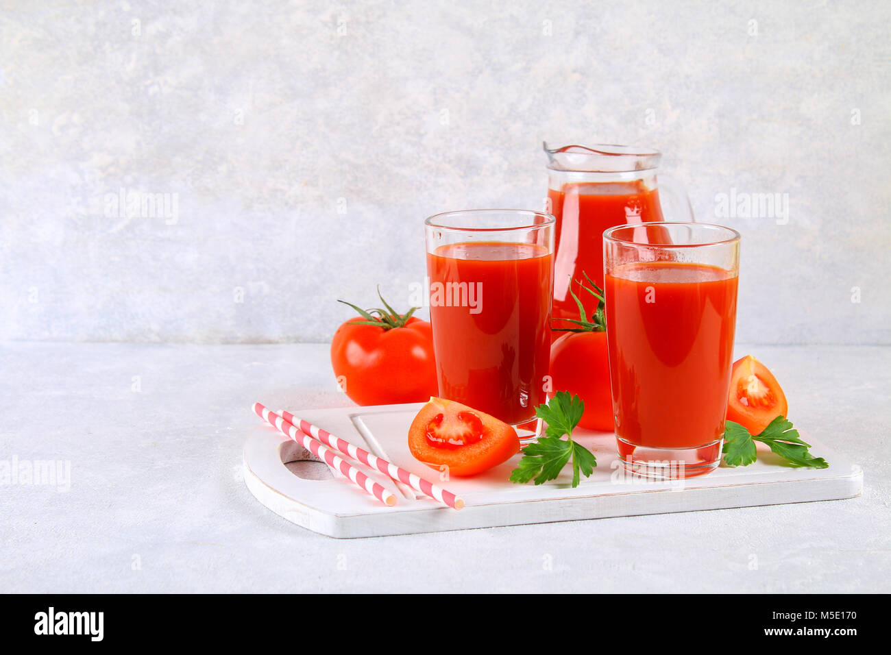 Il succo di pomodoro in bicchieri e una brocca su un calcestruzzo di colore grigio nella tabella Foto Stock