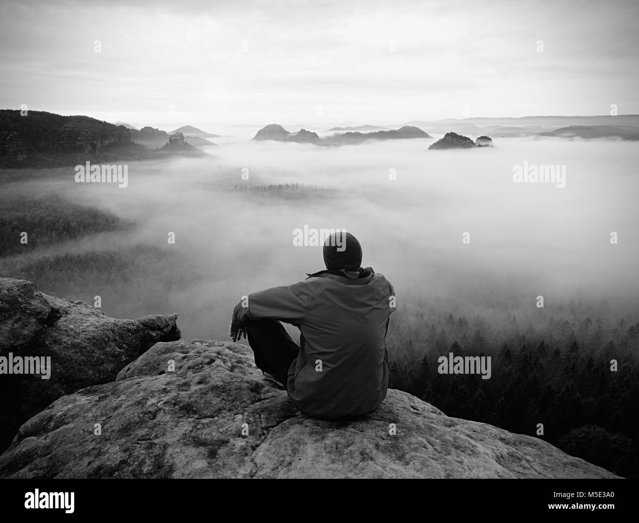 Escursionista su uno sperone roccioso a picco. Splendida alba in montagna, pesante nebbia cremosa nella profonda valle. L'uomo al vertice. Foto in bianco e nero. Foto Stock
