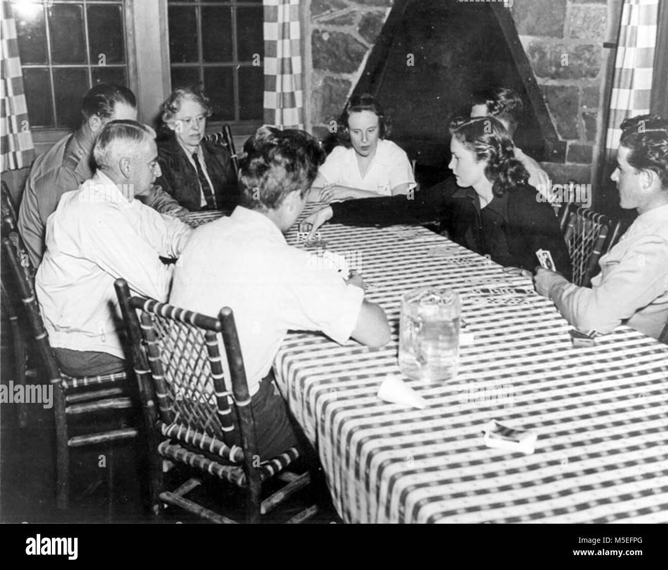 Grand Canyon storica- Phantom Ranch Card Game c Phantom Ranch. Un gioco di cuori rende la serata interessante al ranch del fantoccio. Gruppo di 8 ospiti seduti intorno a giocare a carte al tavolo nella sala da pranzo. Camino dietro. Circa 1950, Foto Stock