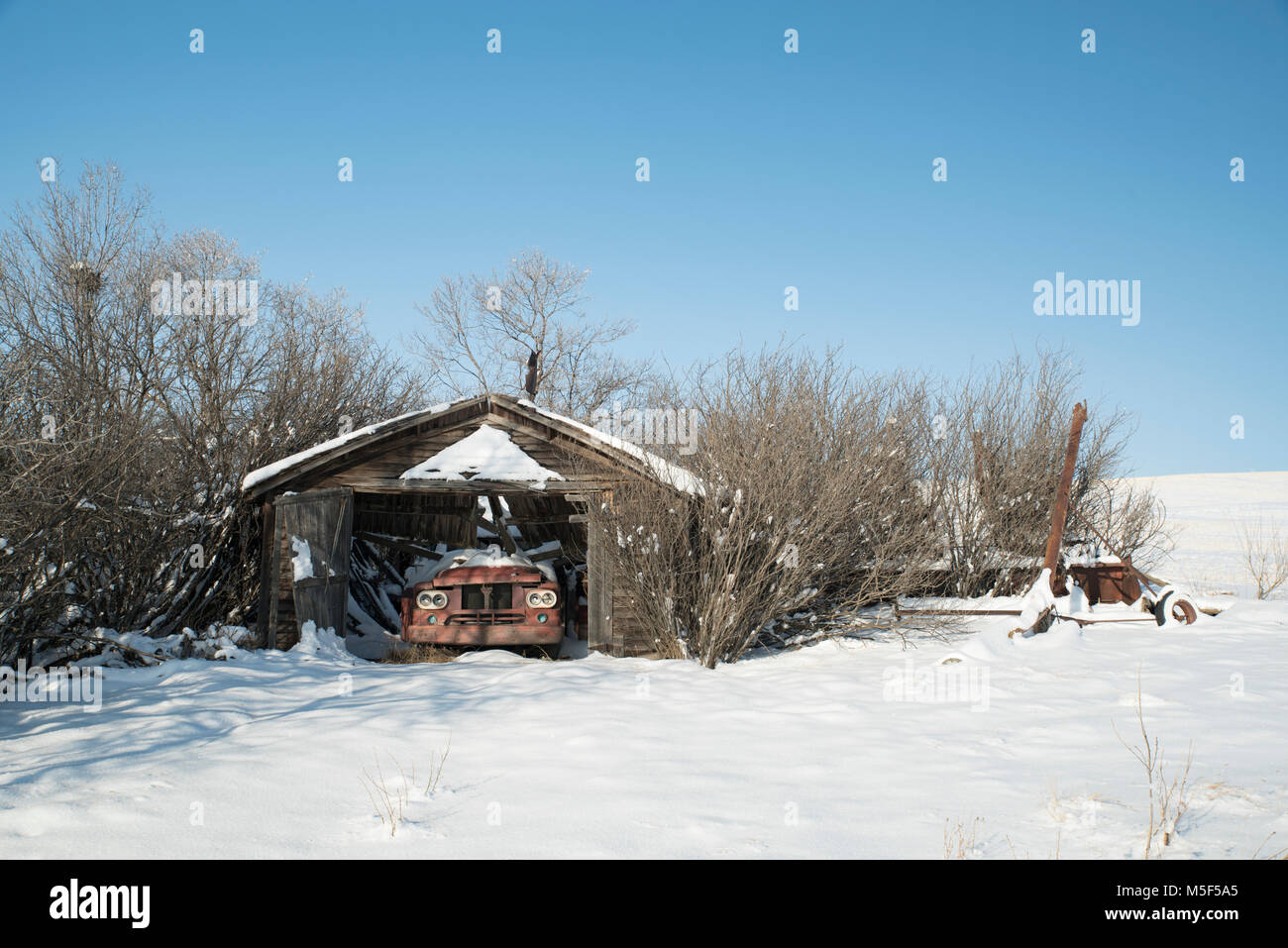 La Contea di Wheatland, Alberta, Canada. Abbandonato garage da cortile con tetto è crollato sul carrello di antiquariato nella prateria in inverno. Foto Stock