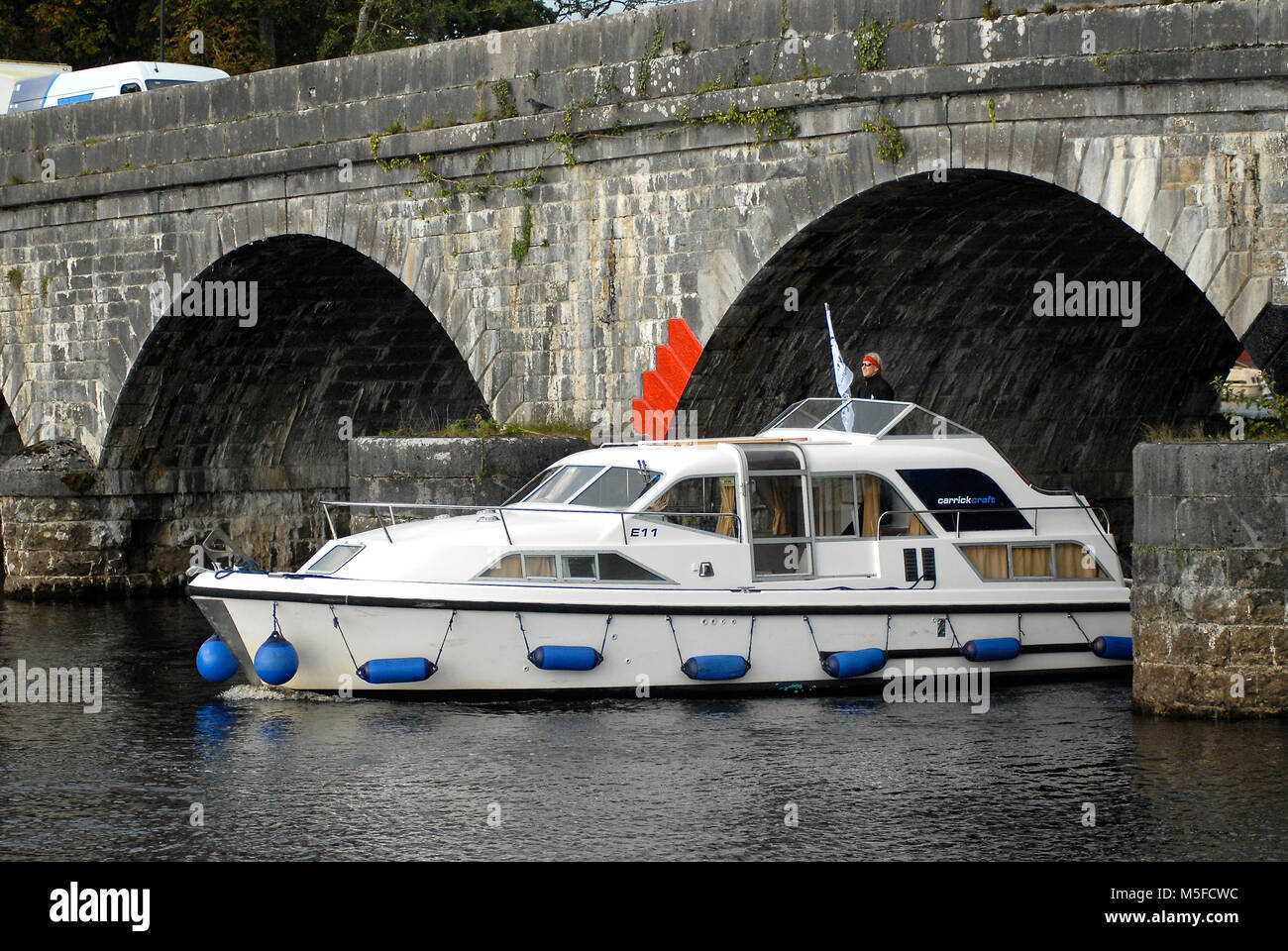 A Carrick Craft motor cruiser passa sotto il ponte di Carrick-on-Shannon, sul fiume Shannon, che collega Co Leitrim e Co Roscommon, Irlanda. Foto Stock