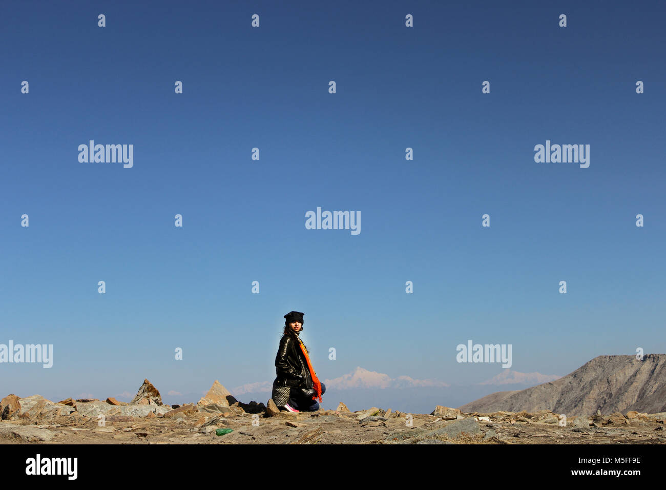 Ragazza seduta sulla cima di una montagna rivolto verso la telecamera, neve sulle montagne e il cielo blu in background Foto Stock