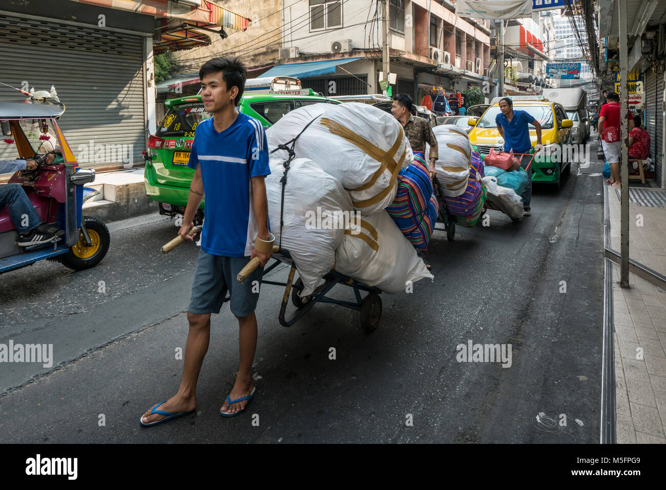 Gli uomini che trasportano merci con un carrello sulla strada di Bangkok Foto Stock