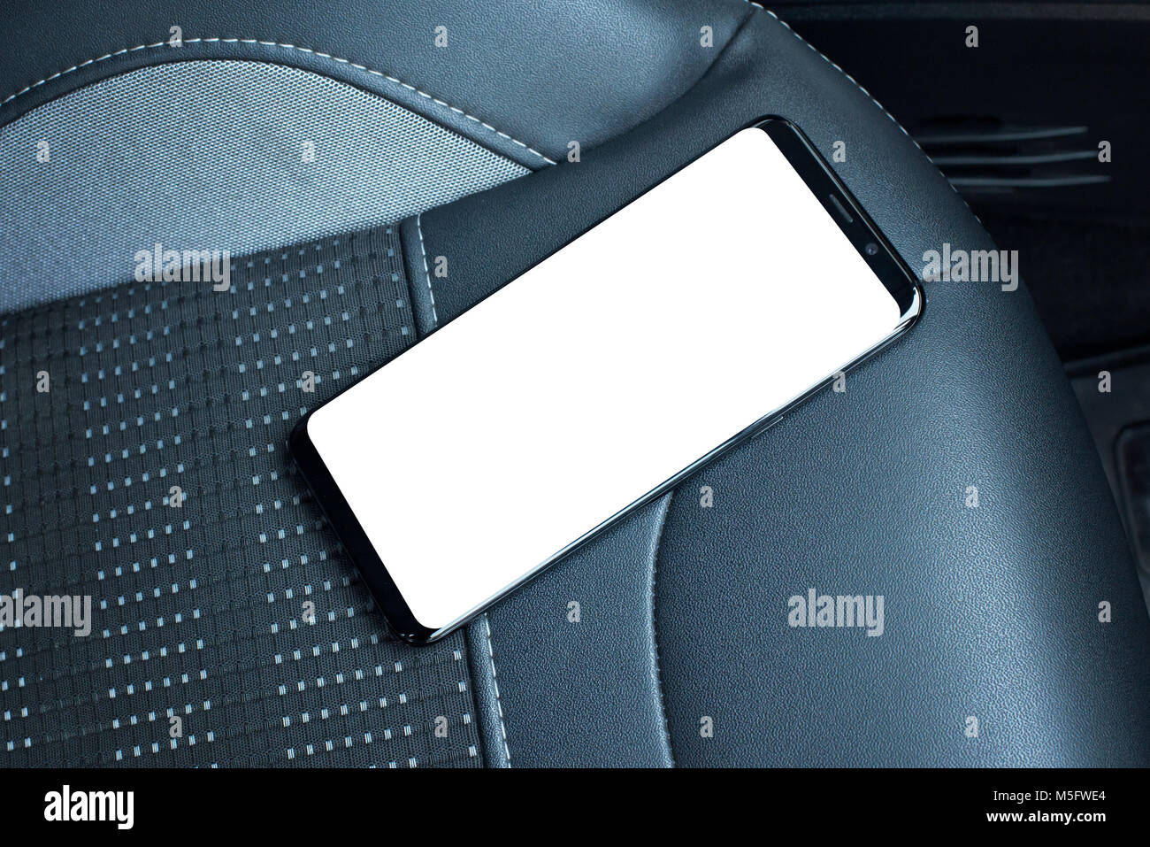 Telefono cellulare sul sedile auto. Schermo isolato per mockup. In cuoio nero sedile in background. Foto Stock