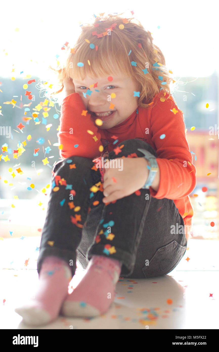 Timida ragazzina dai capelli rossi seduto sotto sparkle coriandoli nel giorno del suo compleanno, sorridente e divertirsi. Foto Stock